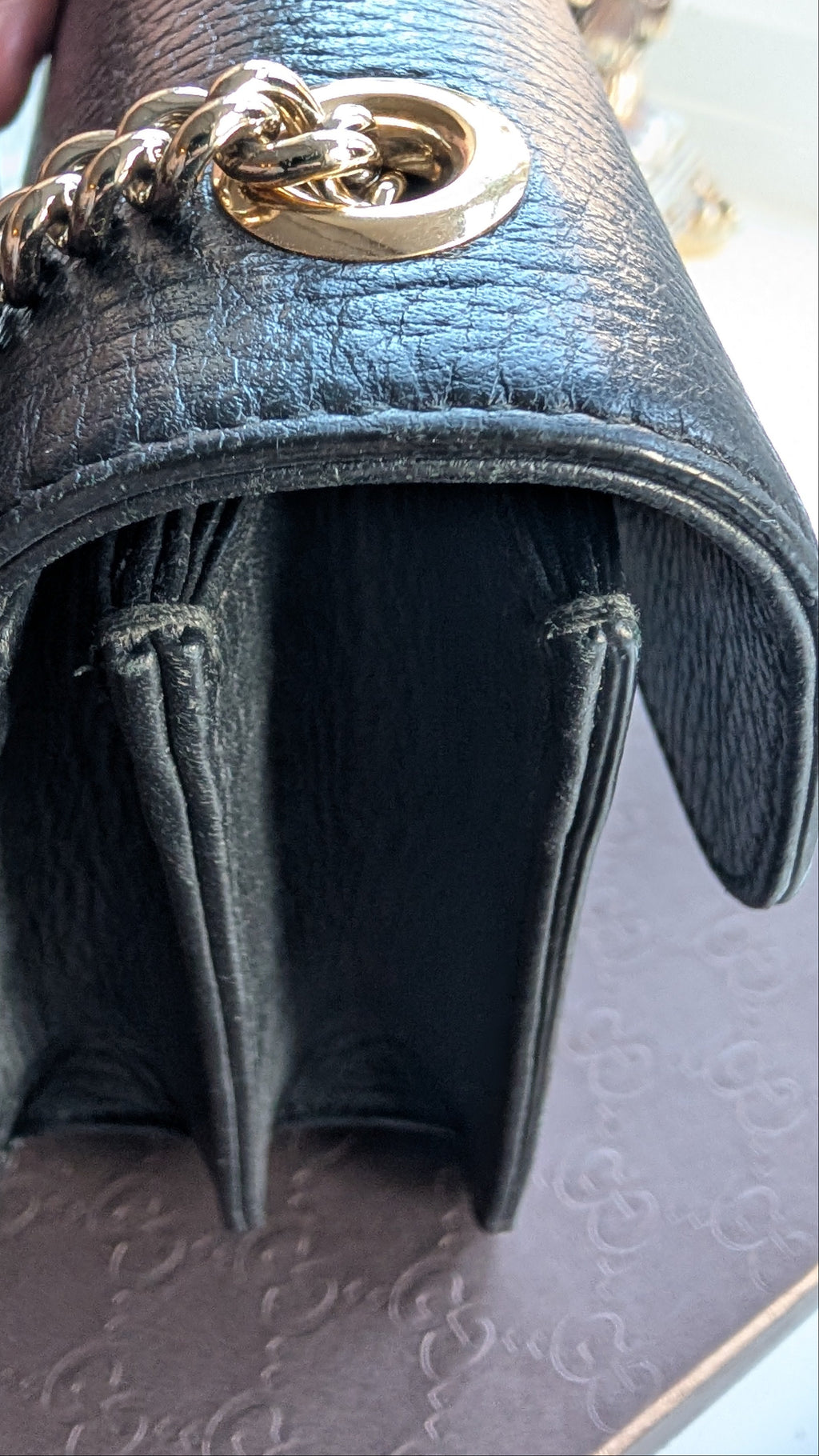 Close-up of a black leather handbag with a gold-tone chain strap and ring detail, held by a hand over a patterned surface. Pre-Owned Gucci Interlocking Black shoulder bag 