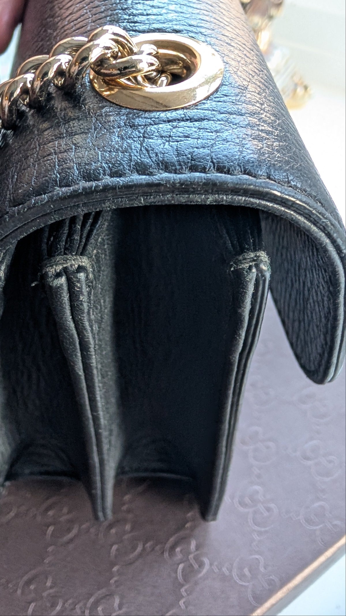 Close-up of a black leather handbag with a gold-tone chain strap and ring detail, held by a hand over a patterned surface. Pre-Owned Gucci Interlocking Black shoulder bag 