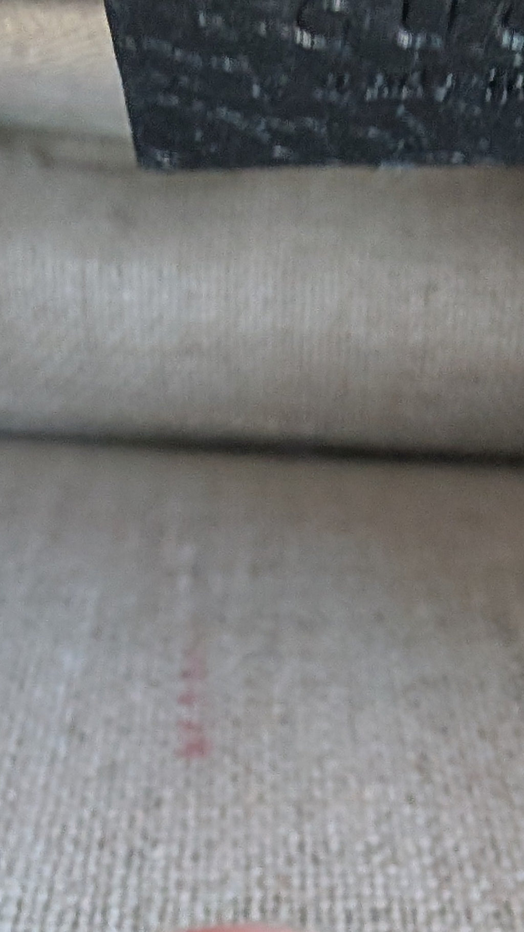 A close-up shot of a beige woven fabric surface with a human finger in the foreground and a dark textured label or strap at the top. Pre-Owned Gucci Interlocking Black shoulder bag 