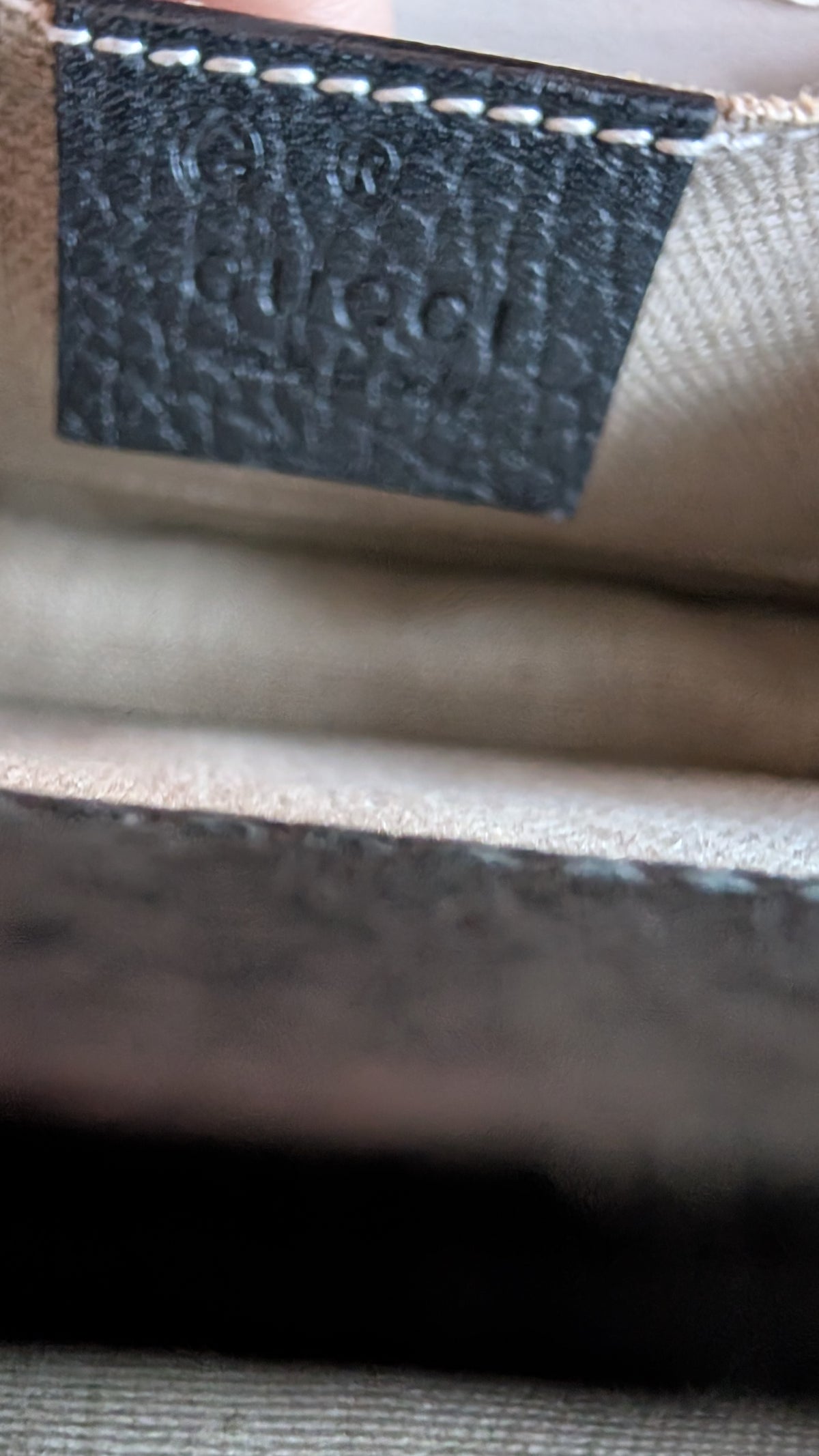Close-up of a Gucci interior label patch on a beige woven fabric surface, with a dark gray stitched leather tab embossed with the Gucci name. Pre-Owned Gucci Interlocking Black shoulder bag 