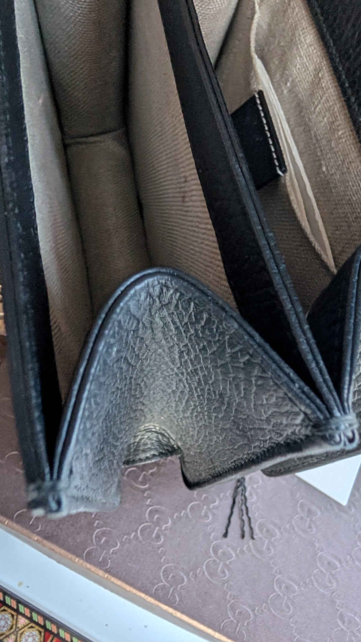 Close-up of a black textured leather zippered open, revealing beige fabric lining compartments, photographed on a patterned surface. Pre-Owned Gucci Interlocking Black shoulder bag 