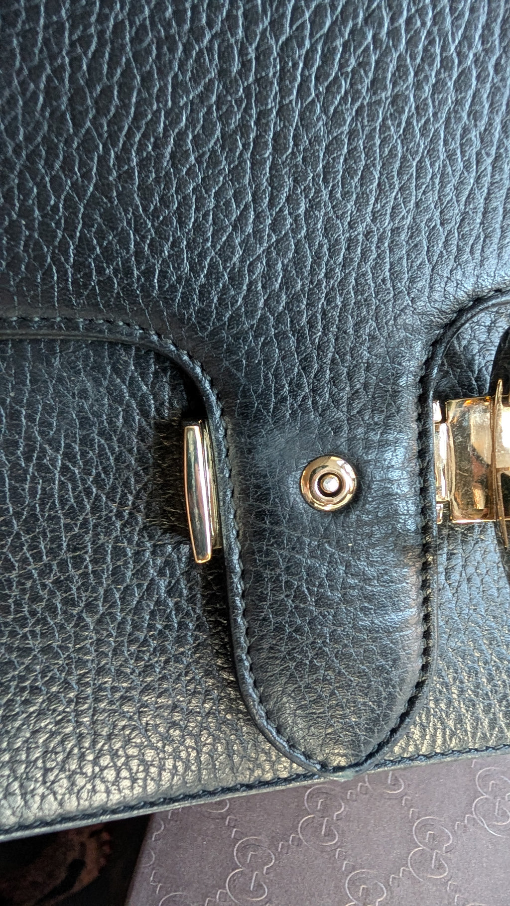 Close-up of a dark pebbled leather handbag showing a snap button closure with gold-toned hardware. Pre-Owned Gucci Interlocking Black shoulder bag 