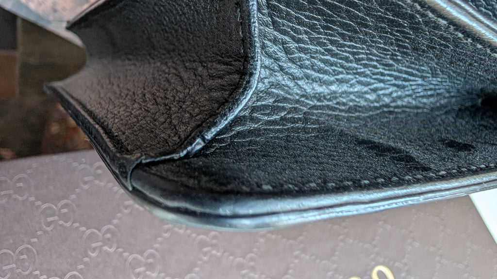 Close-up of a black textured leather item, showing the grain and stitching detail, resting on a patterned brown surface. Pre-Owned Gucci Interlocking Black shoulder bag 