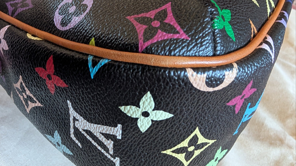 Close-up of a Louis Vuitton monogram bag in black coated canvas with colorful printed monogram motifs and a brown leather trim, held by a hand on a light fabric surface. Pre-Owned Louis Vuitton Takashi Murakami Lodge PM Shoulder Bag