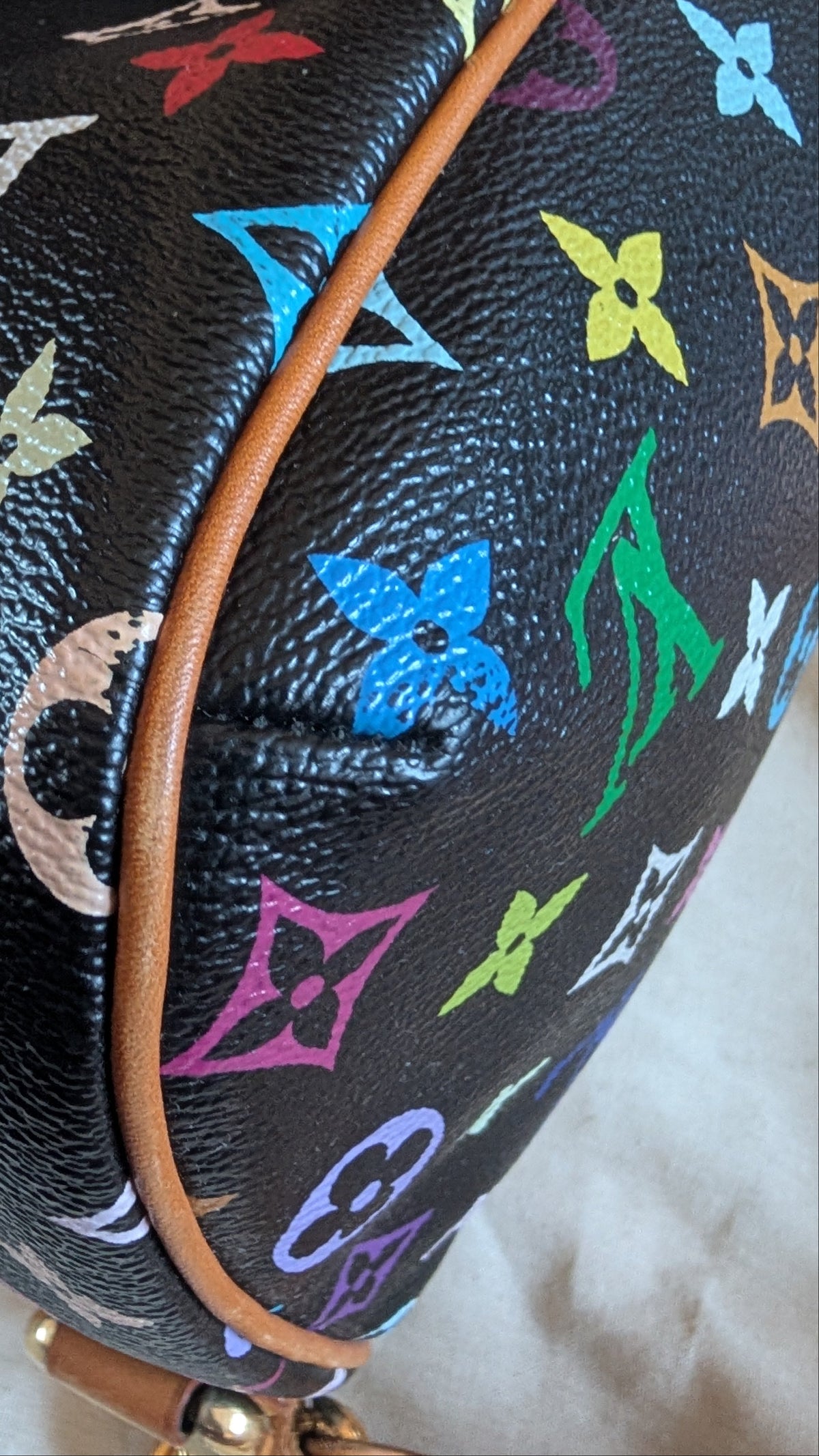 Close-up of a Louis Vuitton monogram bag in black coated canvas with multicolor printed monogram motifs and a tan leather trim, held by a hand. Pre-Owned Louis Vuitton Takashi Murakami Lodge PM Shoulder Bag