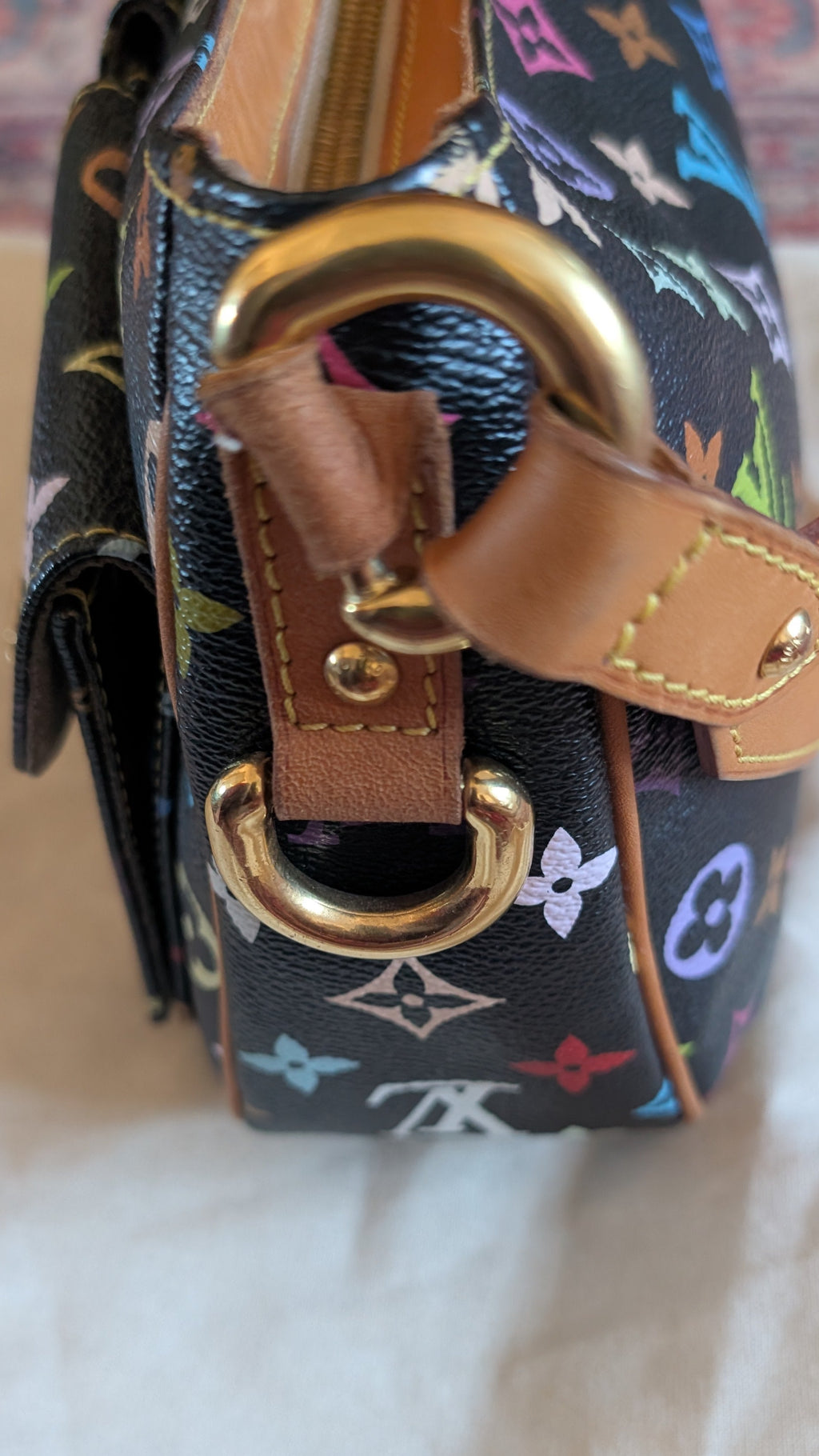 A close-up of a Louis Vuitton shoulder bag featuring the classic multicolor monogram canvas, tan leather strap, and gold-tone hardware, resting on a light-colored fabric surface. Pre-Owned Louis Vuitton Takashi Murakami Lodge PM Shoulder Bag