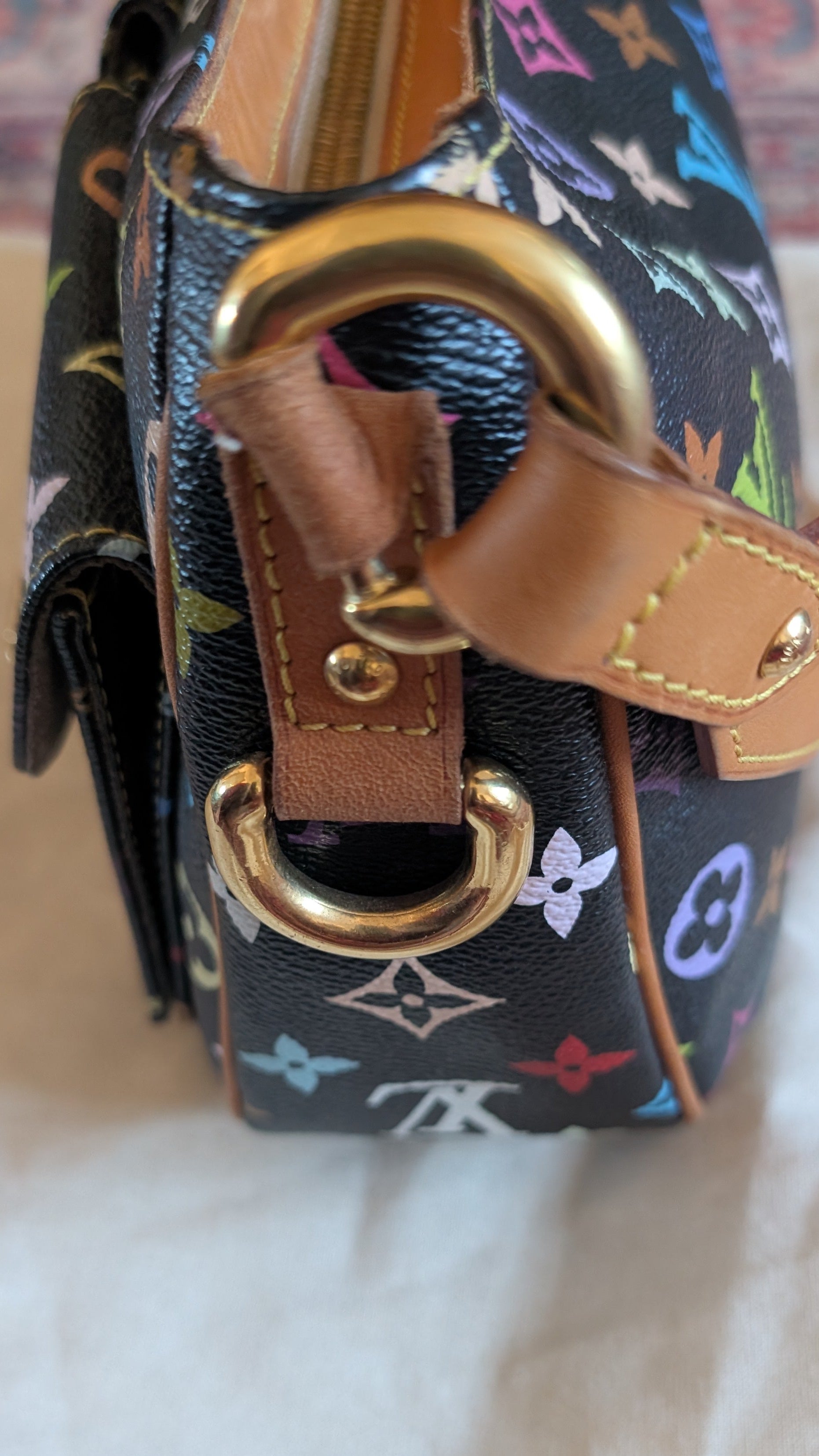 A close-up of a Louis Vuitton shoulder bag featuring the classic multicolor monogram canvas, tan leather strap, and gold-tone hardware, resting on a light-colored fabric surface. Pre-Owned Louis Vuitton Takashi Murakami Lodge PM Shoulder Bag