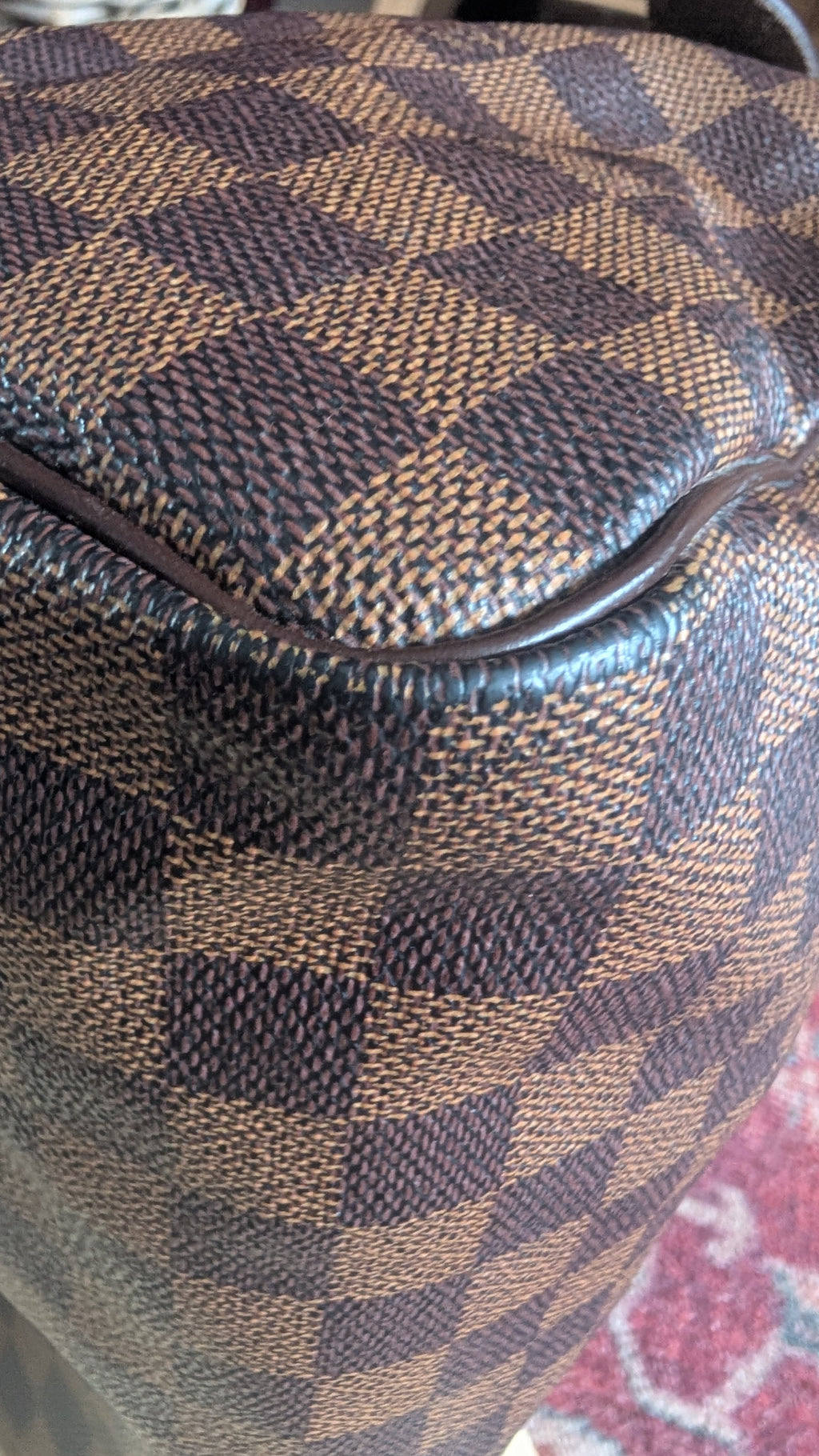 Close-up of a brown and tan checkered fabric surface with a dark zipper line, showing the textured woven pattern. Pre-Owned Louis Vuitton Speedy 25 in classic Damier Ebene coated canvas