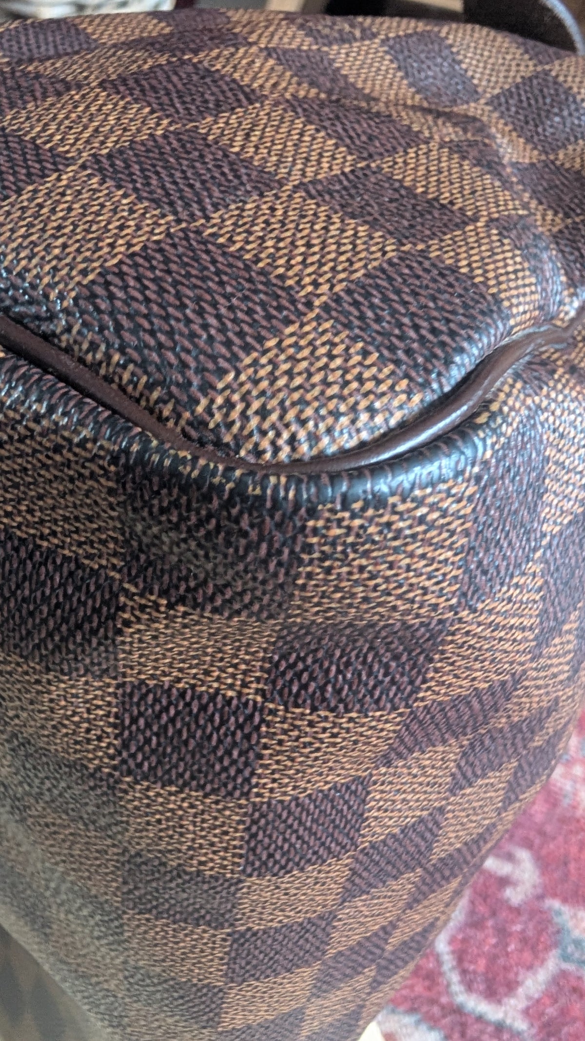 Close-up of a brown and tan checkered fabric surface with a dark zipper line, showing the textured woven pattern. Pre-Owned Louis Vuitton Speedy 25 in classic Damier Ebene coated canvas