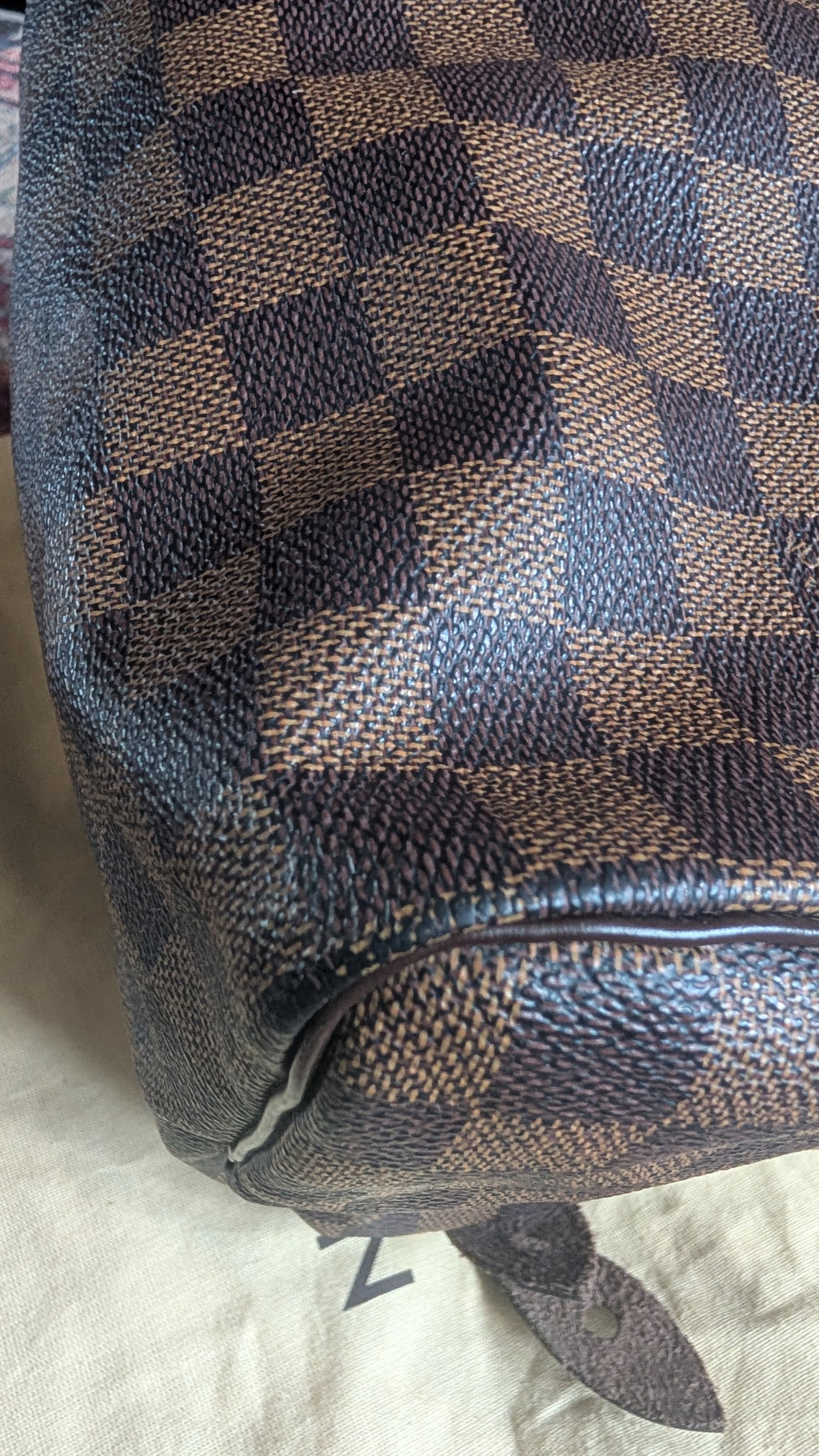 Close-up of a Louis Vuitton Damier Ebene canvas bag, showing the classic dark brown and tan checkerboard pattern with pebbled leather texture. Pre-Owned Louis Vuitton Speedy 25 in classic Damier Ebene coated canvas
