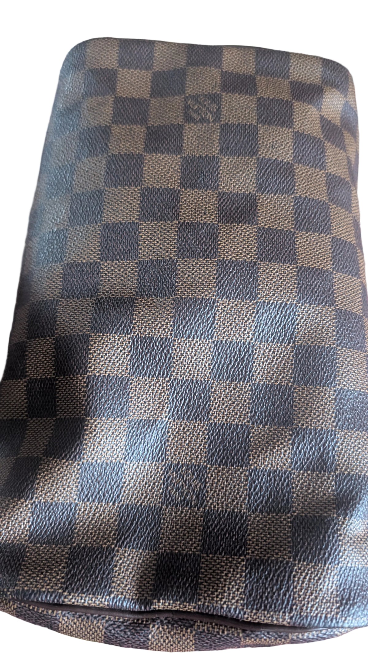 A close-up of a Louis Vuitton handbag or pouch in the Damier Ebene checkered pattern, featuring alternating dark brown and tan squares with a subtle embossed V logo in the center of some squares. Pre-Owned Louis Vuitton Speedy 25 in classic Damier Ebene coated canvas