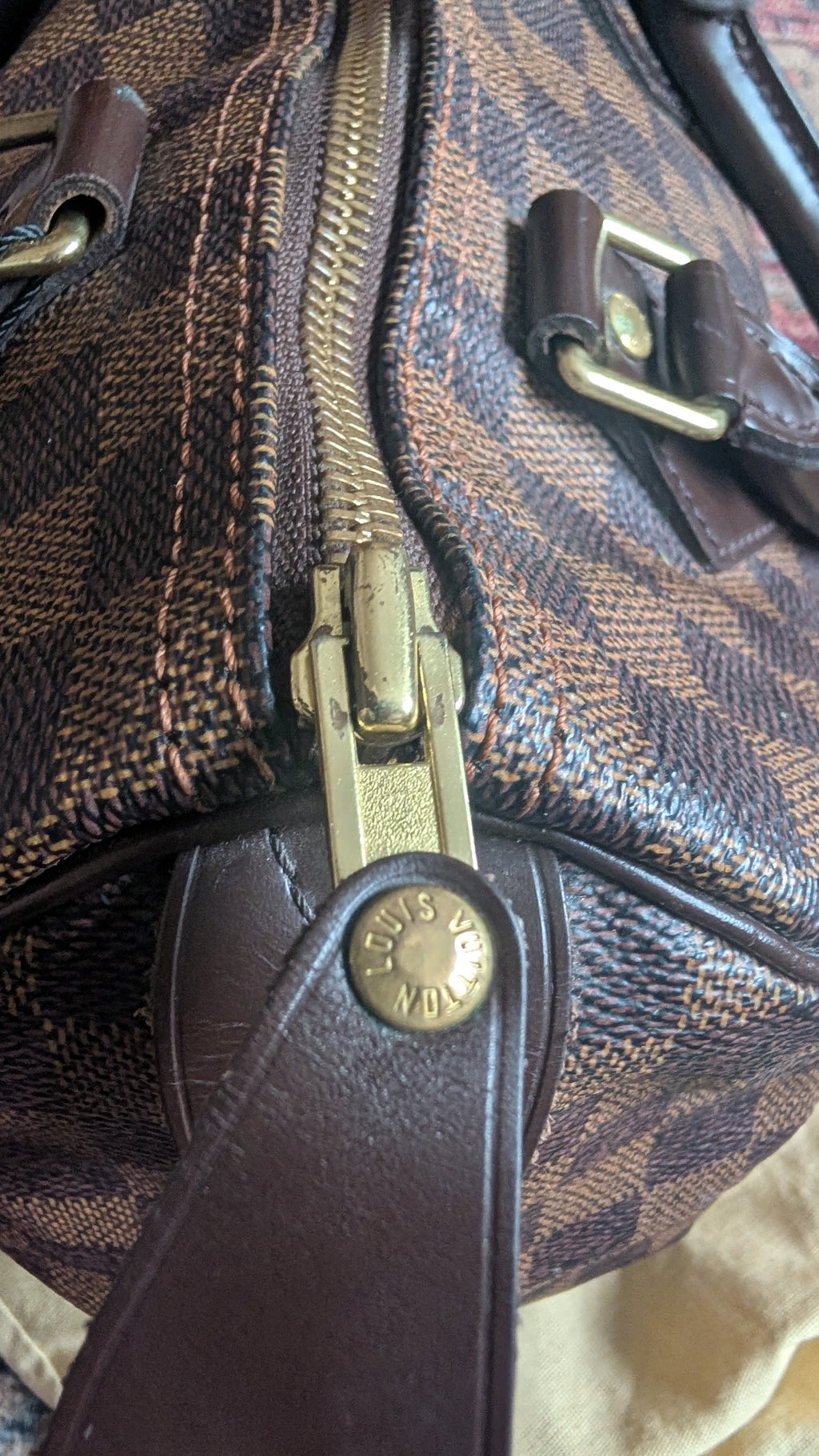 Close-up of a Louis Vuitton monogram canvas bag with brown leather trim, a gold-toned zipper, and a branded metal snap. Pre-Owned Louis Vuitton Speedy 25 in classic Damier Ebene coated canvas