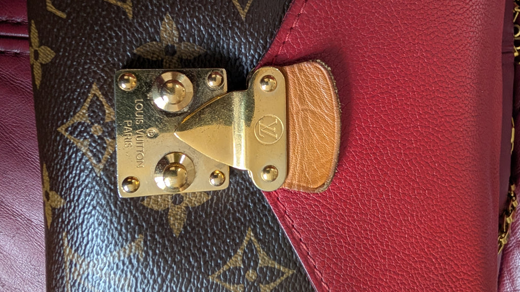 Close-up of a Louis Vuitton handbag showing a brown monogram canvas section, a red leather flap, and a gold-tone metal clasp with a tan leather tab. Pre-Owned Louis Vuitton Pallas Chain Monogram Canvas Shoulder Bag – Cerise Red – M41201