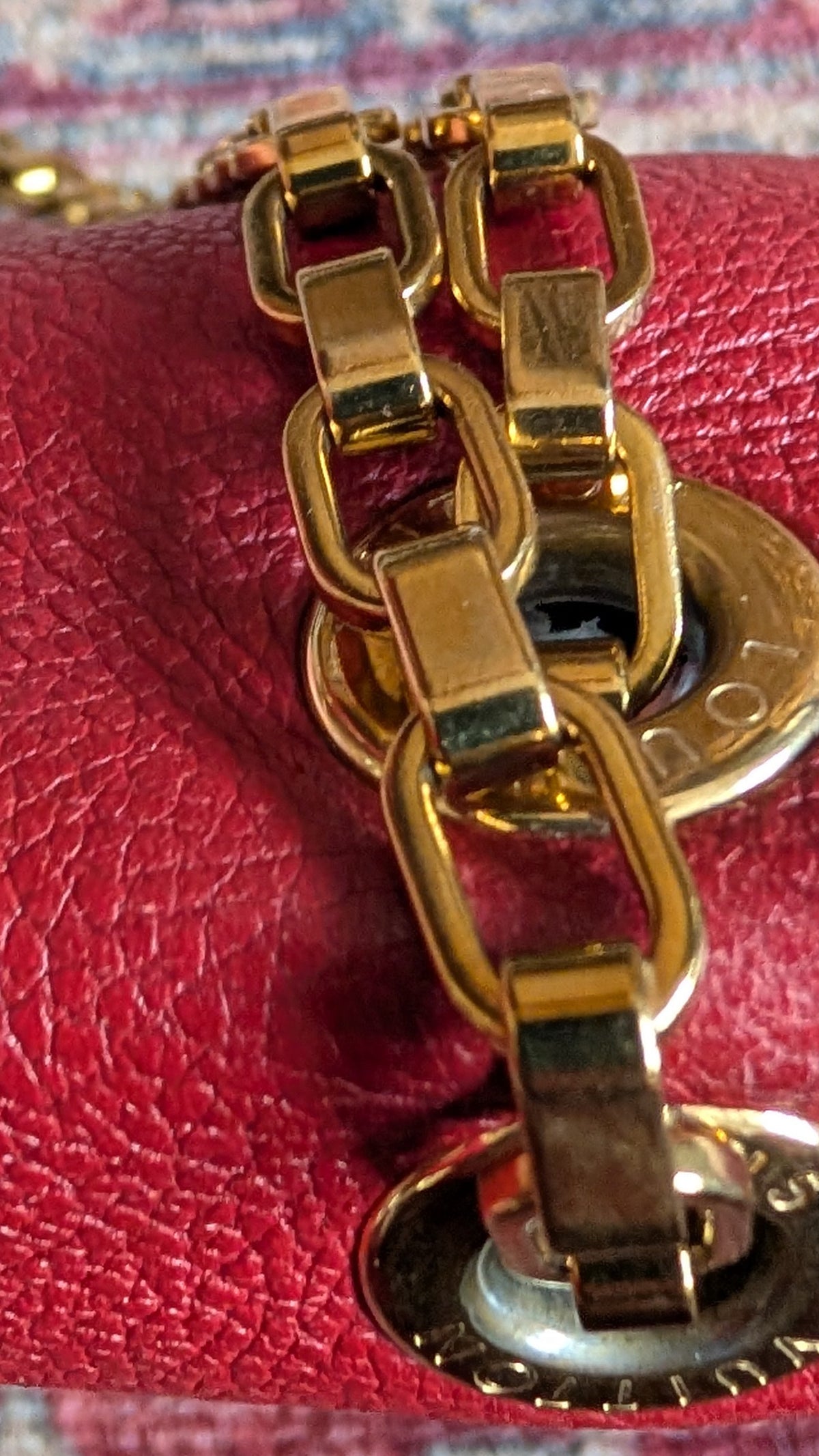 A close-up of a red textured leather handbag featuring a prominent gold-tone chain link strap and circular gold hardware, set against a patterned rug. Pre-Owned Louis Vuitton Pallas Chain Monogram Canvas Shoulder Bag – Cerise Red – M41201