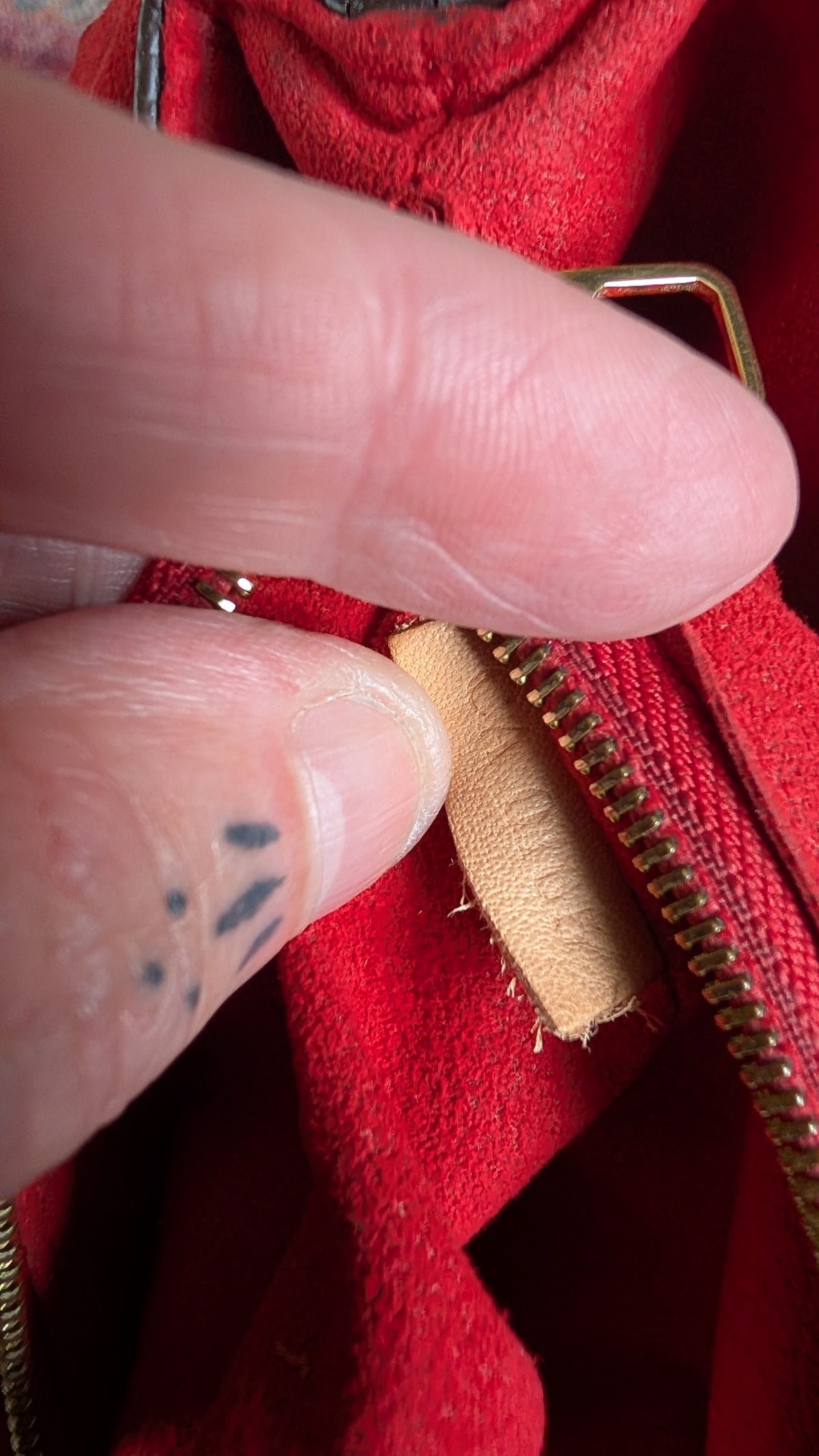 Close-up of a person's fingers pointing to a tan leather zipper pull on a red textured fabric bag with a gold-tone metal zipper. Pre-Owned Louis Vuitton Pallas Chain Monogram Canvas Shoulder Bag – Cerise Red – M41201