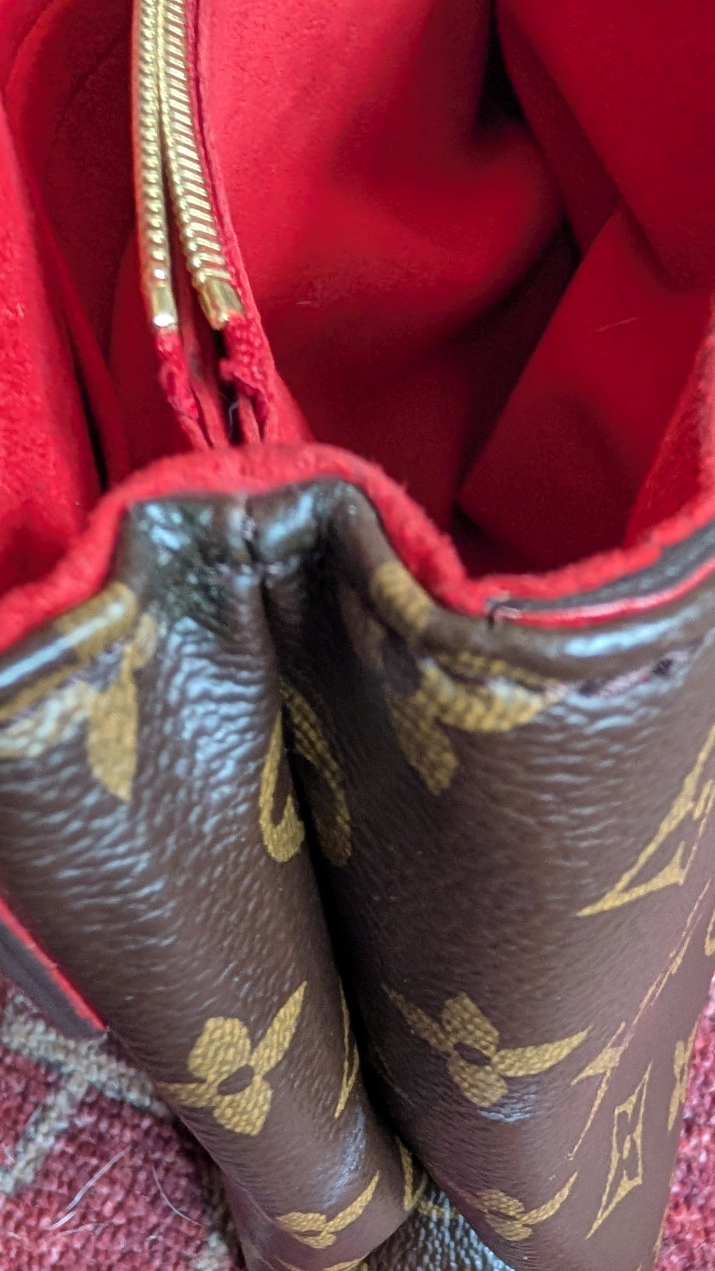 Close-up of a brown Louis Vuitton monogram handbag with a bright red interior lining, resting on a patterned red rug. Pre-Owned Louis Vuitton Pallas Chain Monogram Canvas Shoulder Bag – Cerise Red – M41201