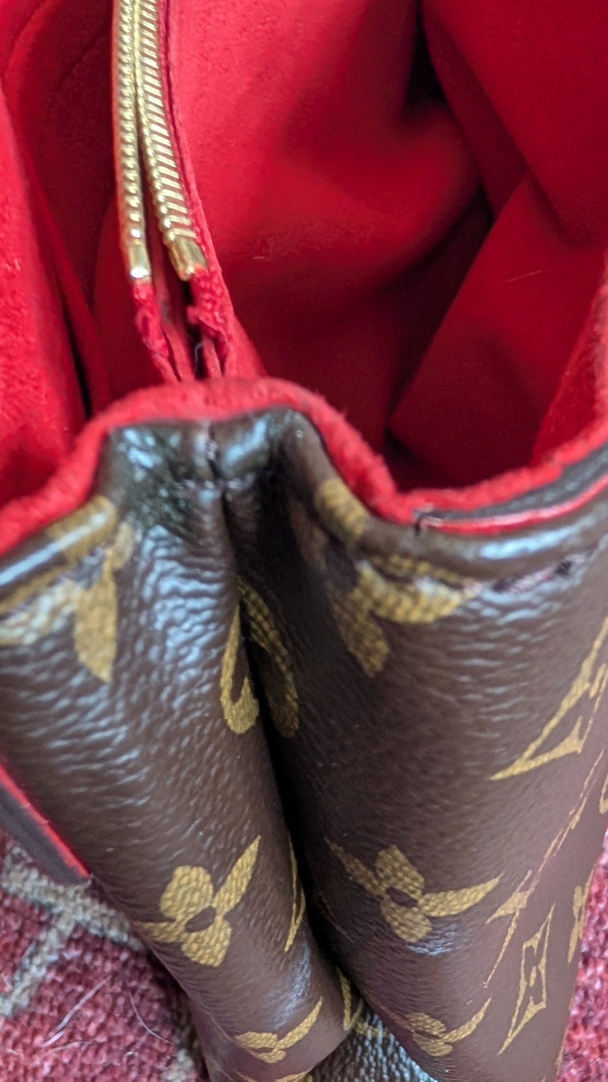 Close-up of a brown Louis Vuitton monogram handbag with a bright red interior lining, resting on a patterned red rug. Pre-Owned Louis Vuitton Pallas Chain Monogram Canvas Shoulder Bag – Cerise Red – M41201