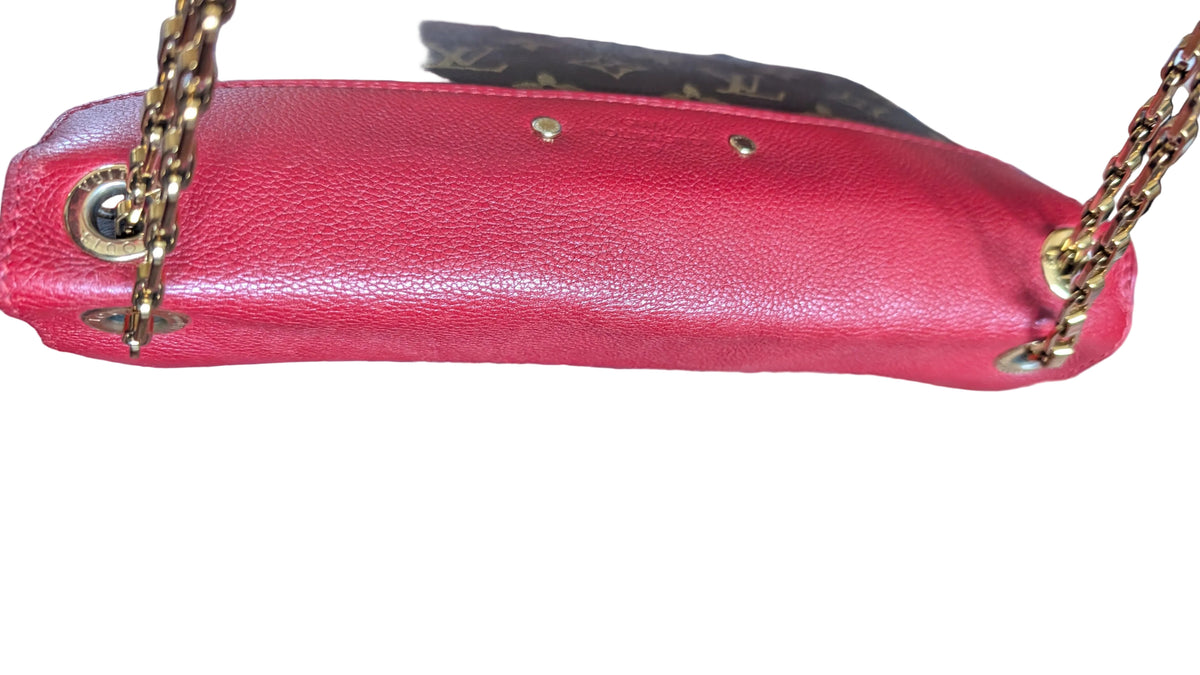 A close-up of a Louis Vuitton shoulder bag in red pebbled leather with gold-tone hardware, shown resting on a patterned red and blue rug. Pre-Owned Louis Vuitton Pallas Chain Monogram Canvas Shoulder Bag – Cerise Red – M41201