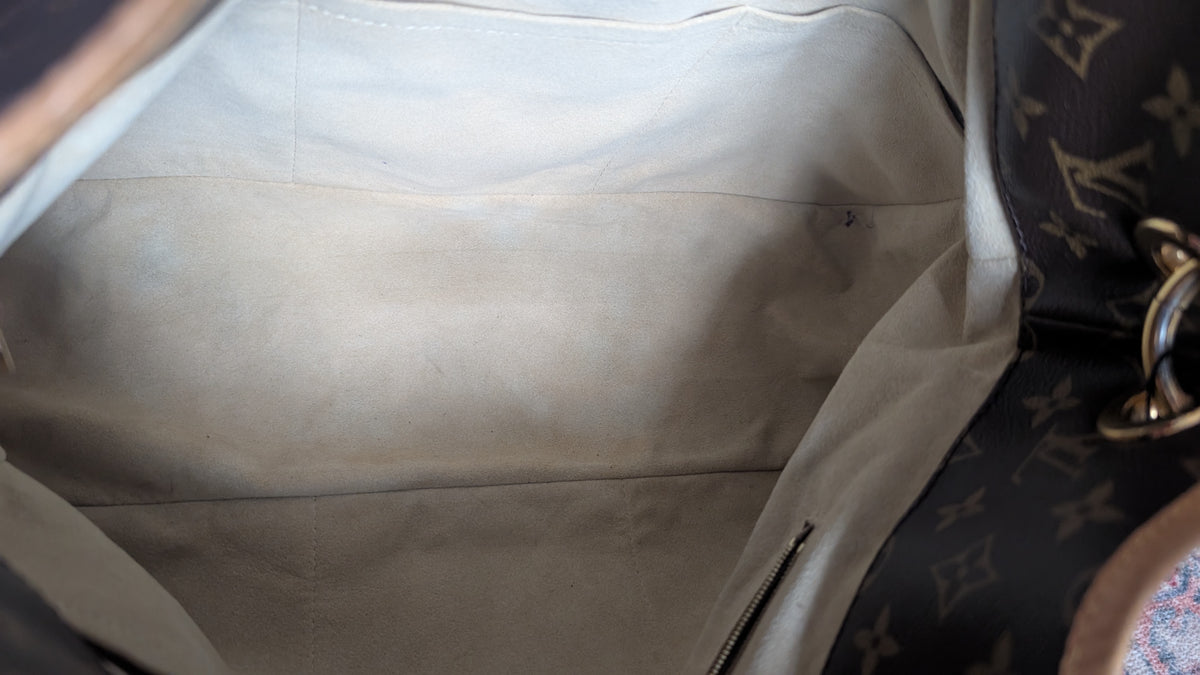 Close-up view of the interior lining of a Louis Vuitton bag, showing a light beige canvas or suede-like interior with a dark brown monogram patterned exterior partially visible on the right side. Pre-Owned Louis Vuitton Artsy MM Monogram Canvas Shoulder Bag 