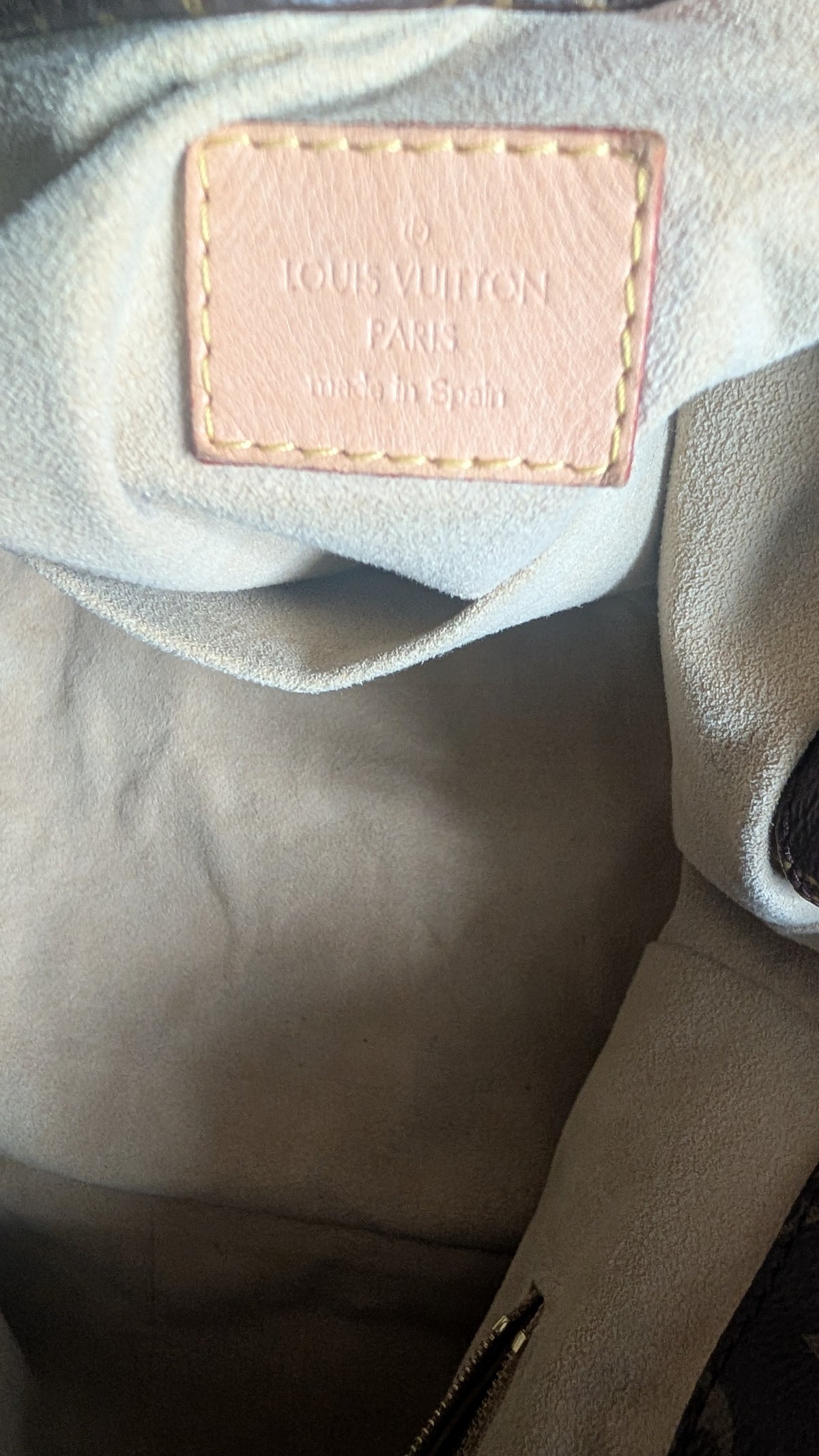 Close-up of the interior of a Louis Vuitton bag, showing a light beige leather brand patch with yellow stitching on a light gray fabric lining. Pre-Owned Louis Vuitton Artsy MM Monogram Canvas Shoulder Bag 