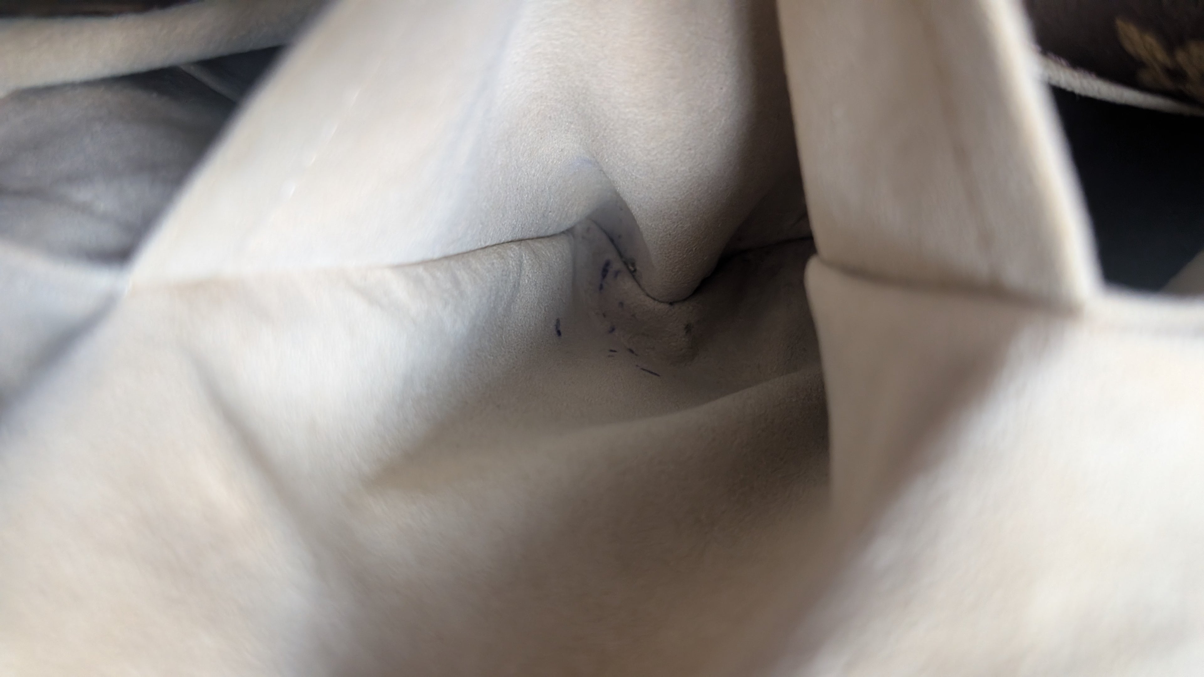 Close-up of a light beige or off-white fabric interior with visible stitching and a small dark stain or scuff near the center. Pre-Owned Louis Vuitton Artsy MM Monogram Canvas Shoulder Bag 