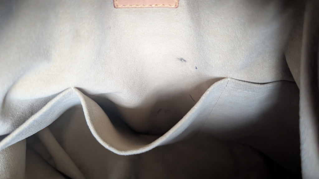 Close-up of the interior lining of a light beige or off-white fabric bag, showing a curved pocket opening and a small stitched leather tab near the top. Pre-Owned Louis Vuitton Artsy MM Monogram Canvas Shoulder Bag 