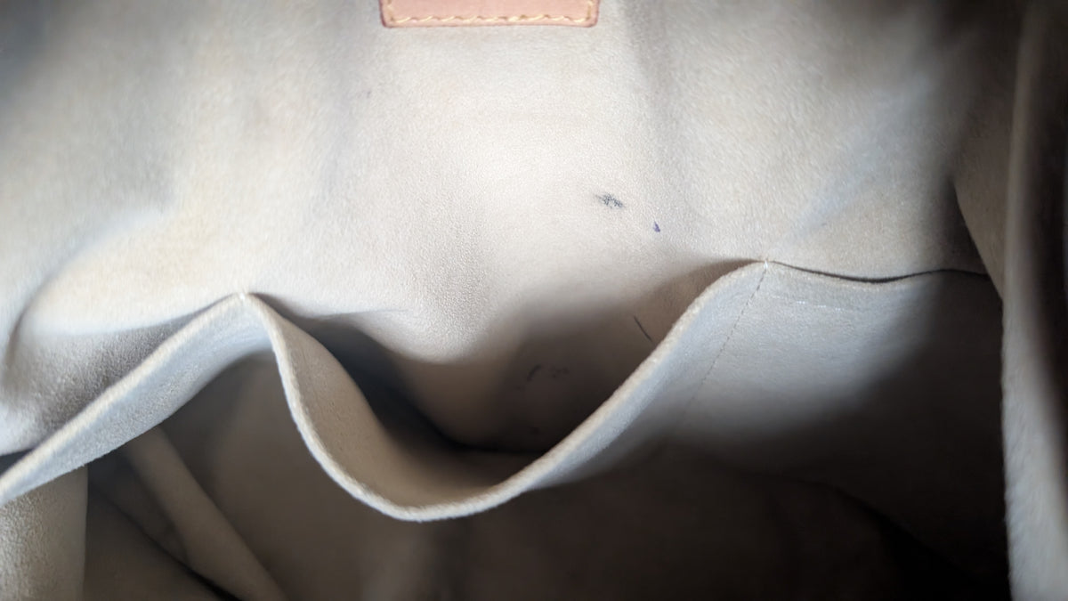 Close-up of the interior lining of a light beige or off-white fabric bag, showing a curved pocket opening and a small stitched leather tab near the top. Pre-Owned Louis Vuitton Artsy MM Monogram Canvas Shoulder Bag 