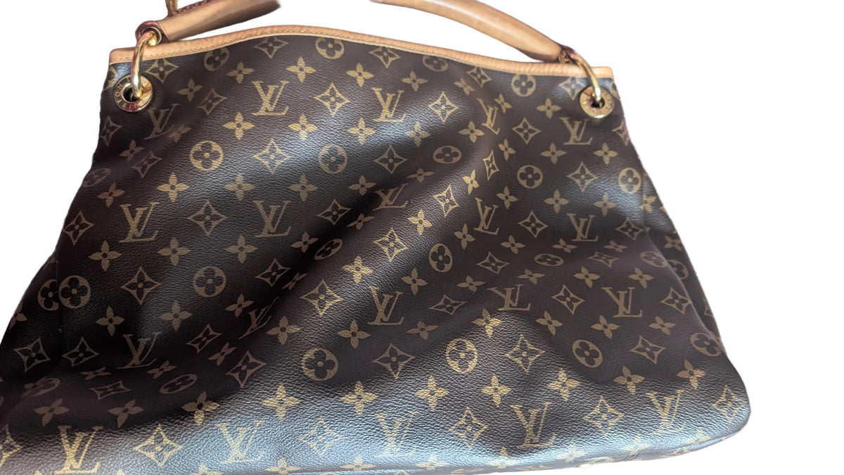 A Louis Vuitton monogram canvas shoulder bag in dark brown with gold-tone hardware, resting on a patterned red and blue rug. Pre-Owned Louis Vuitton Artsy MM Monogram Canvas Shoulder Bag 