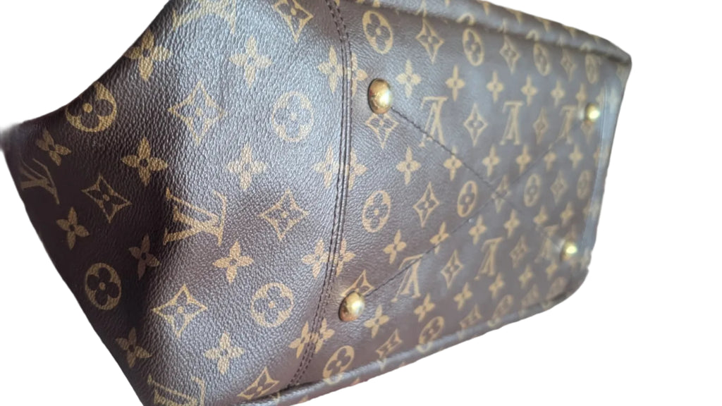 A Louis Vuitton monogram canvas handbag shown from an angled top-down view, resting on a patterned rug. The brown coated canvas features the classic tan/gold LV monogram pattern, with gold-tone metal studs on the side. Pre-Owned Louis Vuitton Artsy MM Monogram Canvas Shoulder Bag 