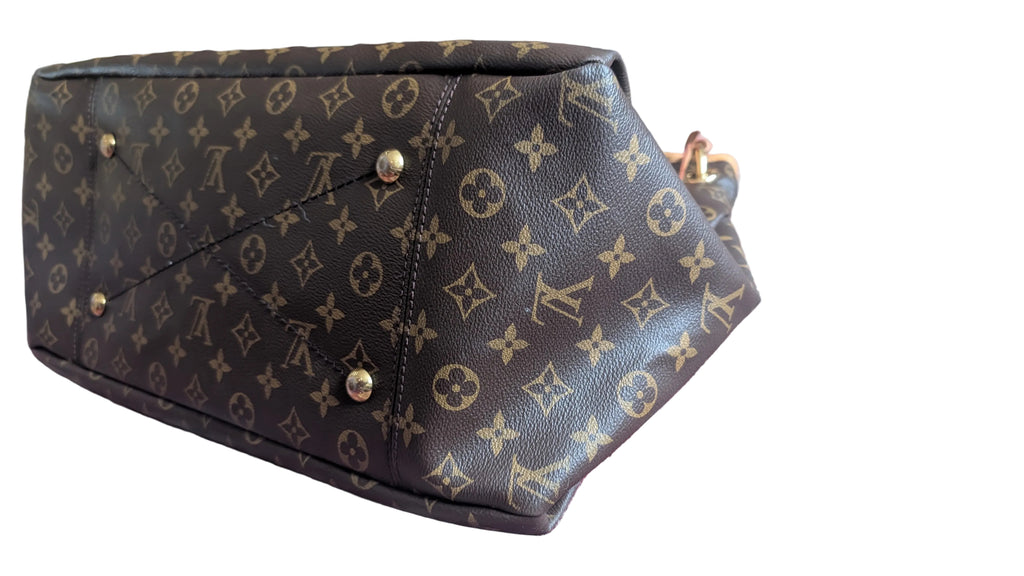 A Louis Vuitton monogram canvas handbag shown from an angled bottom view, resting on a patterned red and blue rug. The dark brown coated canvas features the classic tan monogram pattern with gold-tone metal studs and hardware. Pre-Owned Louis Vuitton Artsy MM Monogram Canvas Shoulder Bag 