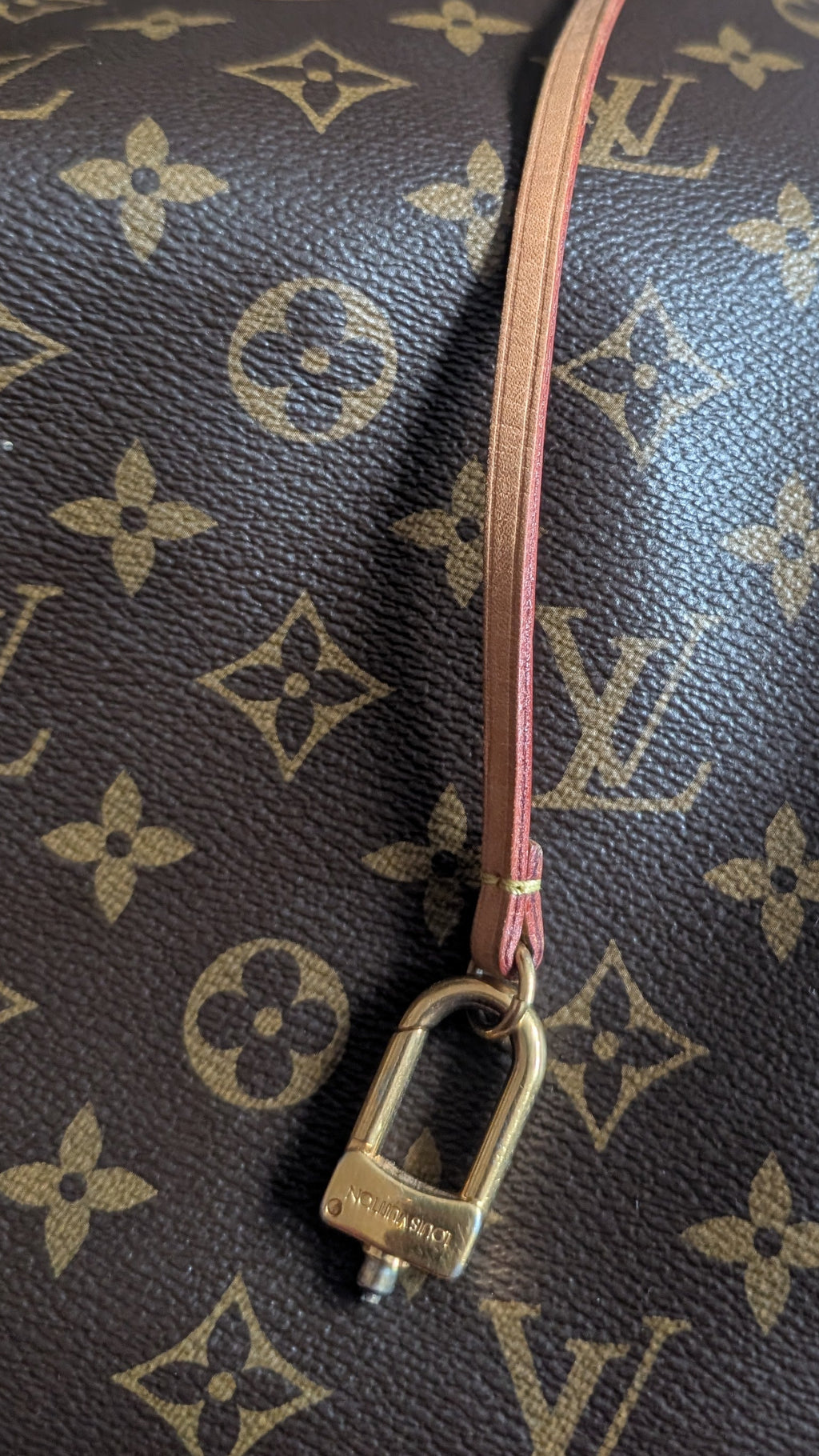 A close-up of a Louis Vuitton monogram canvas bag with a gold-tone padlock charm and a tan leather zipper pull, resting on a patterned rug. Pre-Owned Louis Vuitton Artsy MM Monogram Canvas Shoulder Bag 