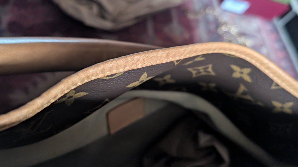 Close-up of the interior lining of a Louis Vuitton monogram handbag, showing the dark brown coated canvas with gold printed monogram motifs and a beige leather trim. Pre-Owned Louis Vuitton Artsy MM Monogram Canvas Shoulder Bag 