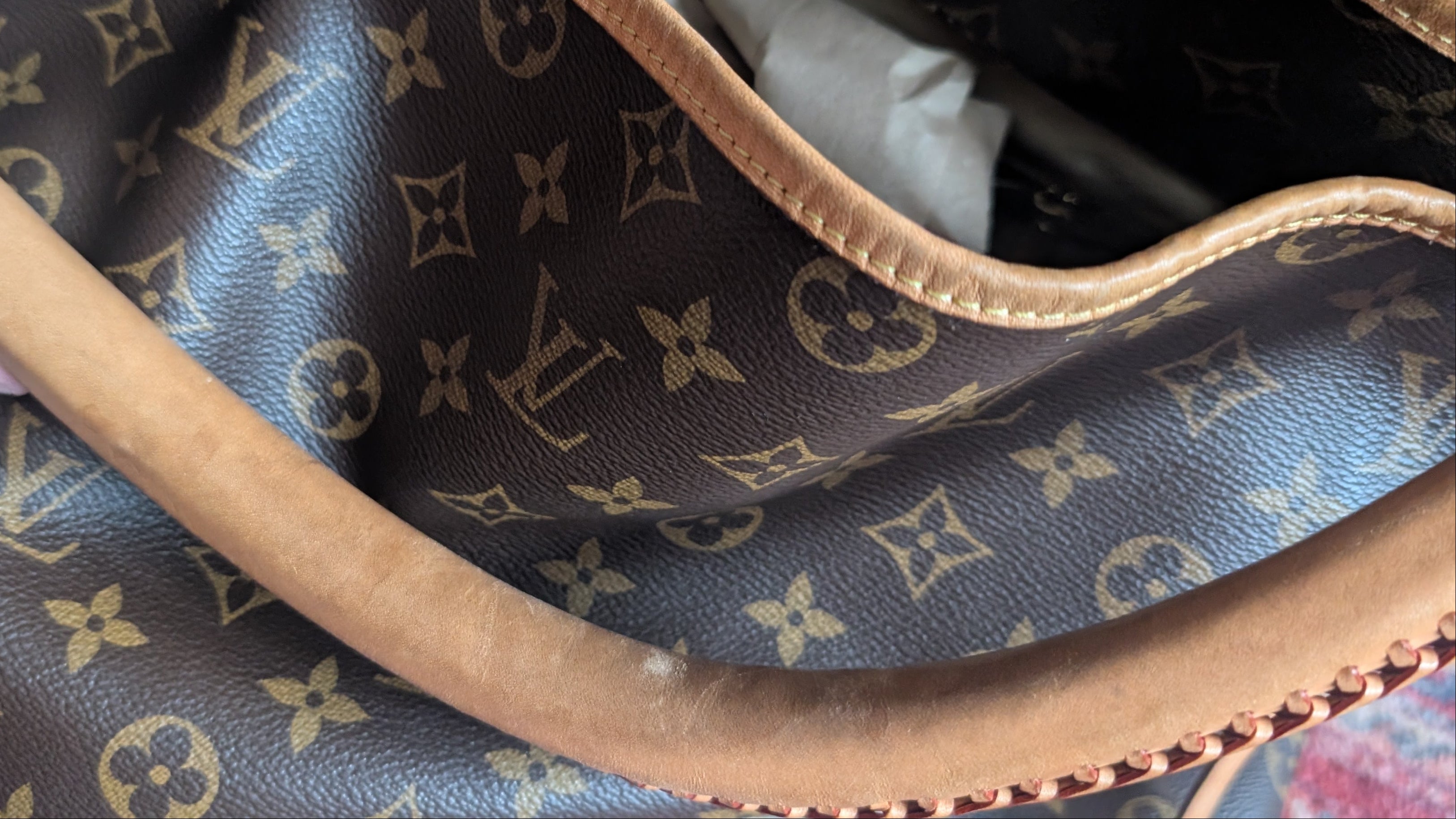 Close-up of a Louis Vuitton monogram canvas handbag with tan leather trim and handle, showing the interior lining and part of a hand holding it open. Pre-Owned Louis Vuitton Artsy MM Monogram Canvas Shoulder Bag 