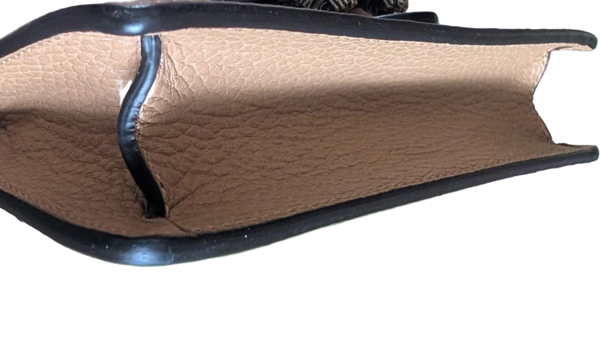 A close-up of a handbag's interior showing a tan pebbled leather lining with black trim, resting on a green textured box over a patterned rug. Pre-Owned Gucci Dionysus Super Mini Crystal Tiger Head Chain Bag – Beige Leather