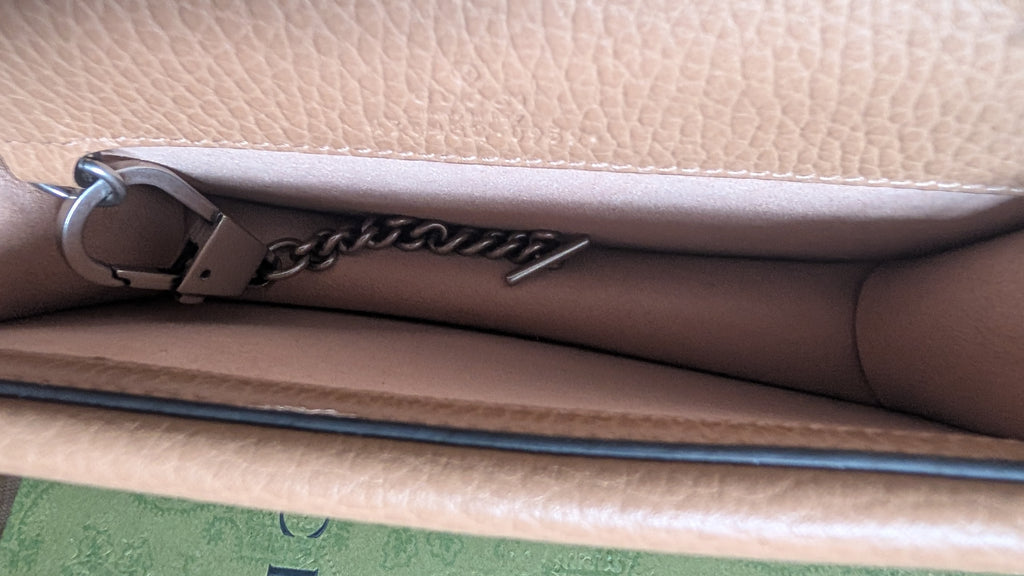 Close-up of the interior of a beige pebbled leather clutch or handbag, showing a silver-tone metal chain detail with a script logo and a silver ring clasp. Pre-Owned Gucci Dionysus Super Mini Crystal Tiger Head Chain Bag – Beige Leather