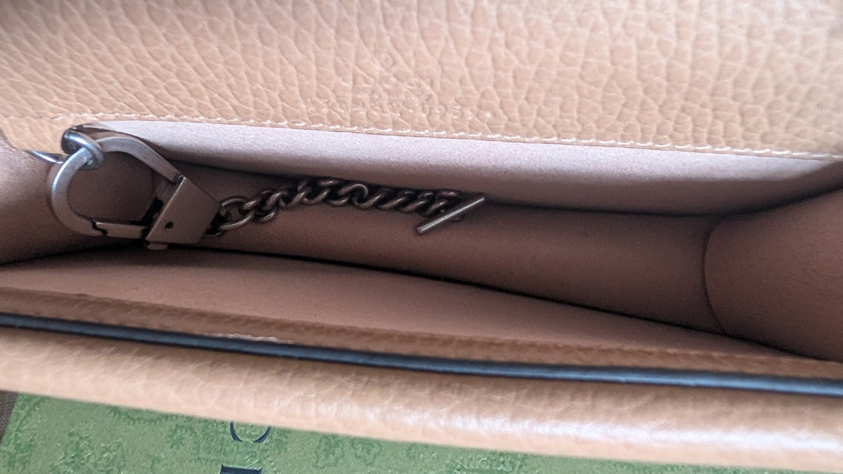 Close-up of the interior of a beige pebbled leather clutch or handbag, showing a silver-tone metal chain detail with a script logo and a silver ring clasp. Pre-Owned Gucci Dionysus Super Mini Crystal Tiger Head Chain Bag – Beige Leather