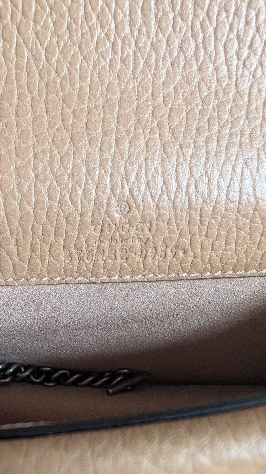 Close-up of a beige pebbled leather surface with a darker brown interior panel, a black chain strap edge, and faint embossed branding. Pre-Owned Gucci Dionysus Super Mini Crystal Tiger Head Chain Bag – Beige Leather