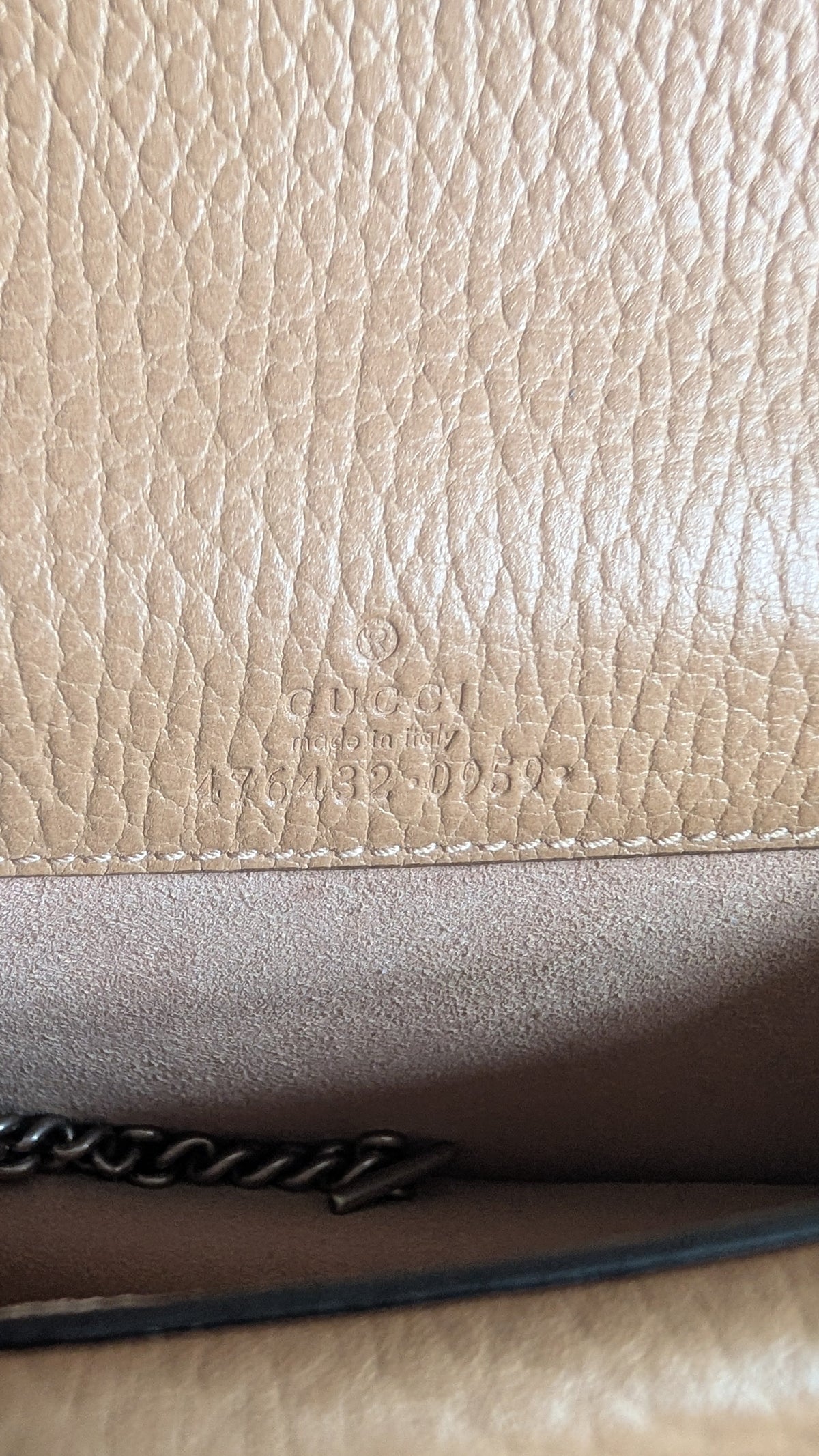 Close-up of a beige pebbled leather surface with a darker brown interior panel, a black chain strap edge, and faint embossed branding. Pre-Owned Gucci Dionysus Super Mini Crystal Tiger Head Chain Bag – Beige Leather