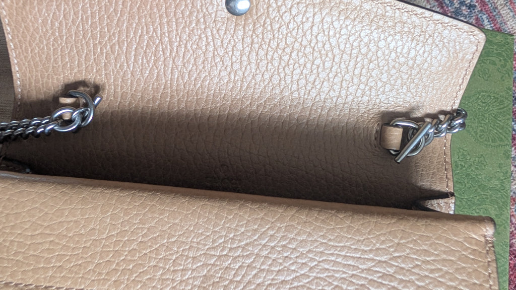 Close-up of a beige pebbled leather clutch or wallet showing the interior lining, silver-tone chain strap attachments, and a metal snap closure. Pre-Owned Gucci Dionysus Super Mini Crystal Tiger Head Chain Bag – Beige Leather