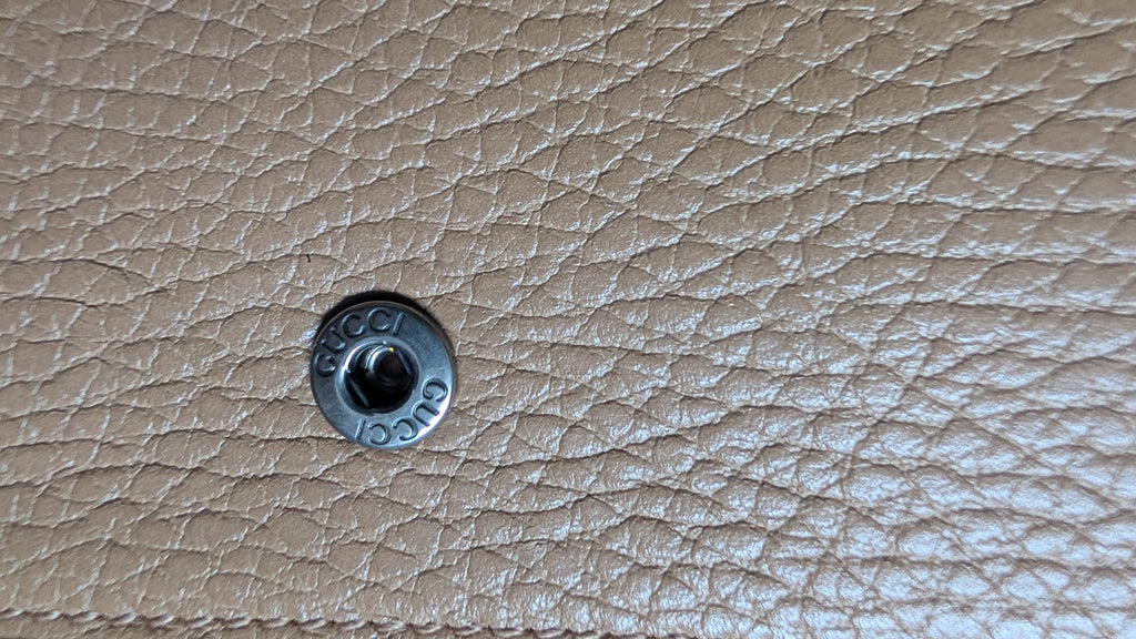 Close-up of a silver-tone metal snap button on a textured beige leather  Pre-Owned Gucci Dionysus Super Mini Crystal Tiger Head Chain Bag – Beige Leathersurface.