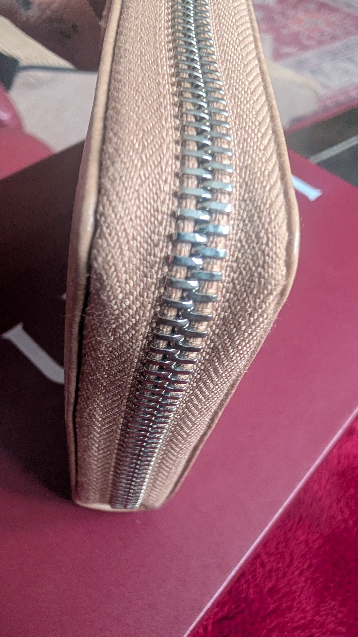 Close-up showing the textured fabric and silver zipper, resting on a dark red surface. Pre-Owned Gucci Interlocking G Zip-Around Continental Purse in Nude/Taupe Leather