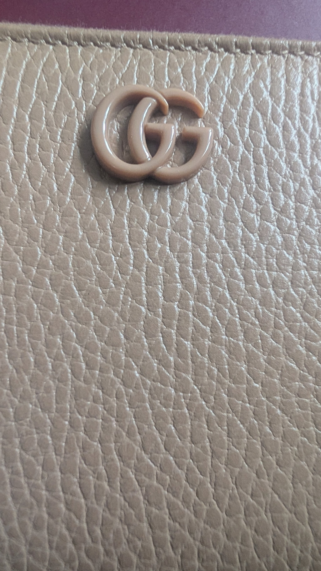 Close-up of a beige pebbled leather item featuring a prominent interlocking GG logo in a matching beige tone, characteristic of Gucci. Pre-Owned Gucci Interlocking G Zip-Around Continental Purse in Nude/Taupe Leather