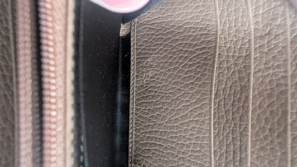 Close-up of a textured leather interior panel in taupe, showing stitching, a black fabric lining, and part of a zipper. Pre-Owned Gucci Interlocking G Zip-Around Continental Purse in Nude/Taupe Leather