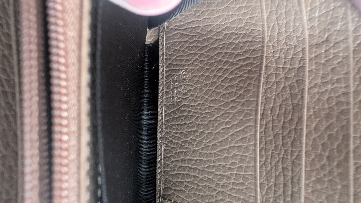 Close-up of a textured leather interior panel in taupe, showing stitching, a black fabric lining, and part of a zipper. Pre-Owned Gucci Interlocking G Zip-Around Continental Purse in Nude/Taupe Leather