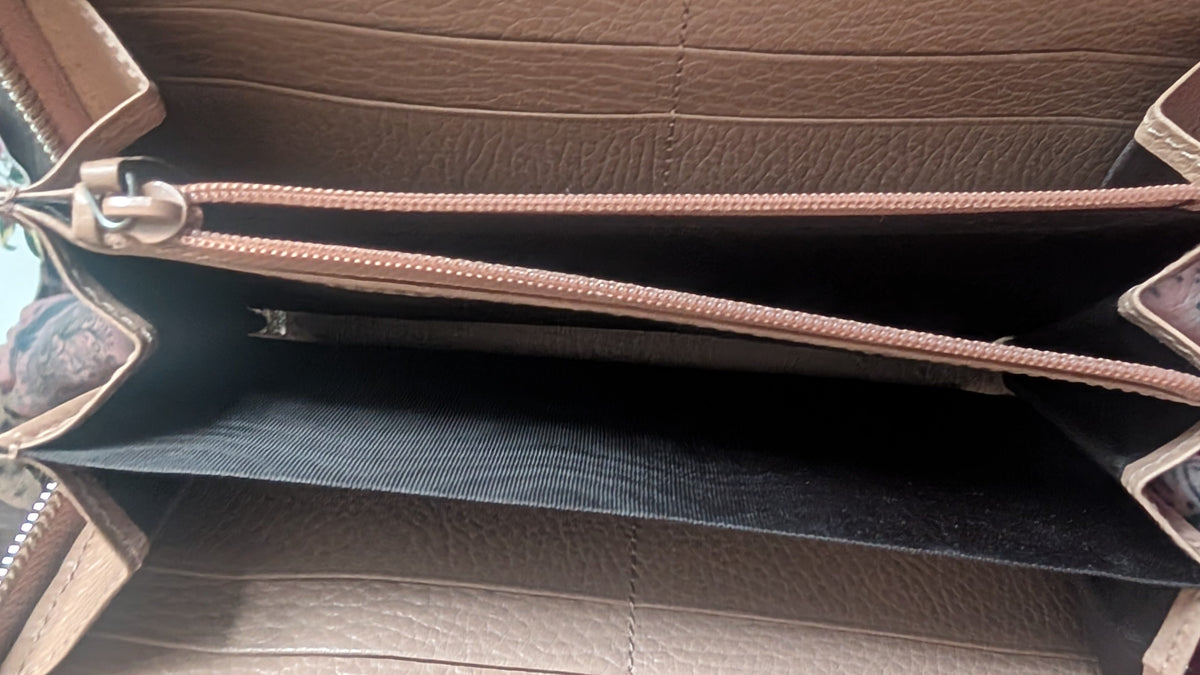 Close-up of the interior of a tan leather wallet or organizer, showing multiple zip compartments, card slots, and a black fabric divider. Pre-Owned Gucci Interlocking G Zip-Around Continental Purse in Nude/Taupe Leather