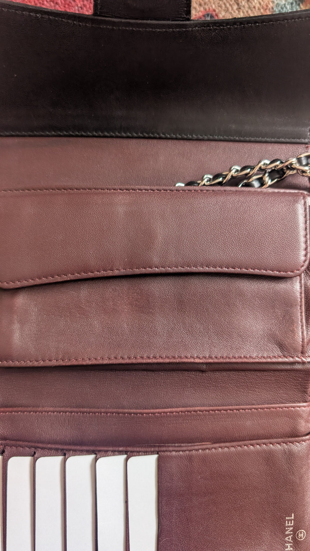 Close-up of a brown leather clutch or wallet with multiple card slots, a flap pocket, and a gold chain detail, shown against a dark background. Pre-Owned Chanel Classic Wallet on Chain WOC – Black Quilted Lambskin