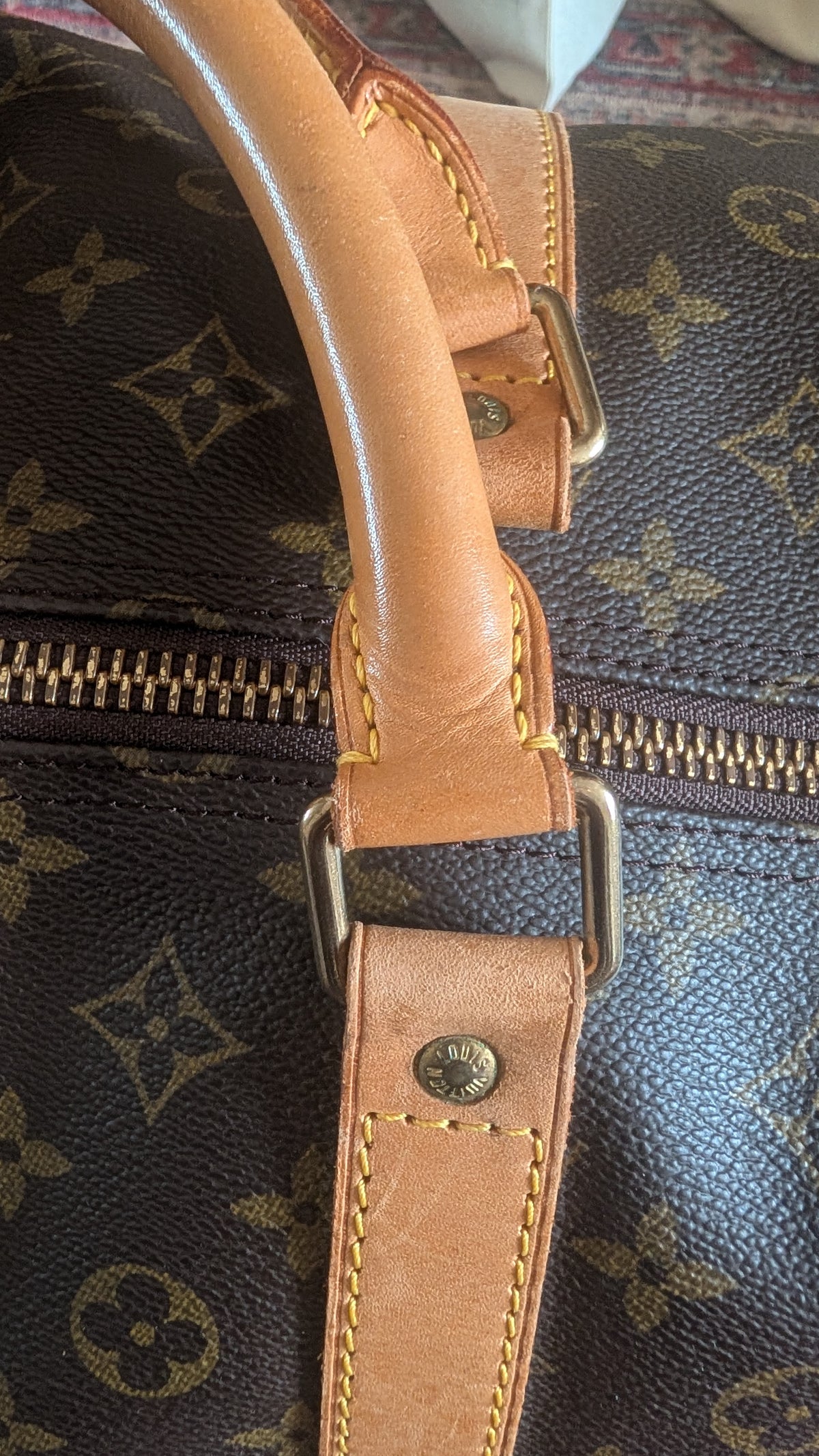 Close-up of a brown monogram duffel bag with tan leather handles and zipper details, showing the Louis Vuitton monogram pattern and metal hardware. Pre-Owned Louis Vuitton Keepall Bandoulière 60 Monogram Travel Bag