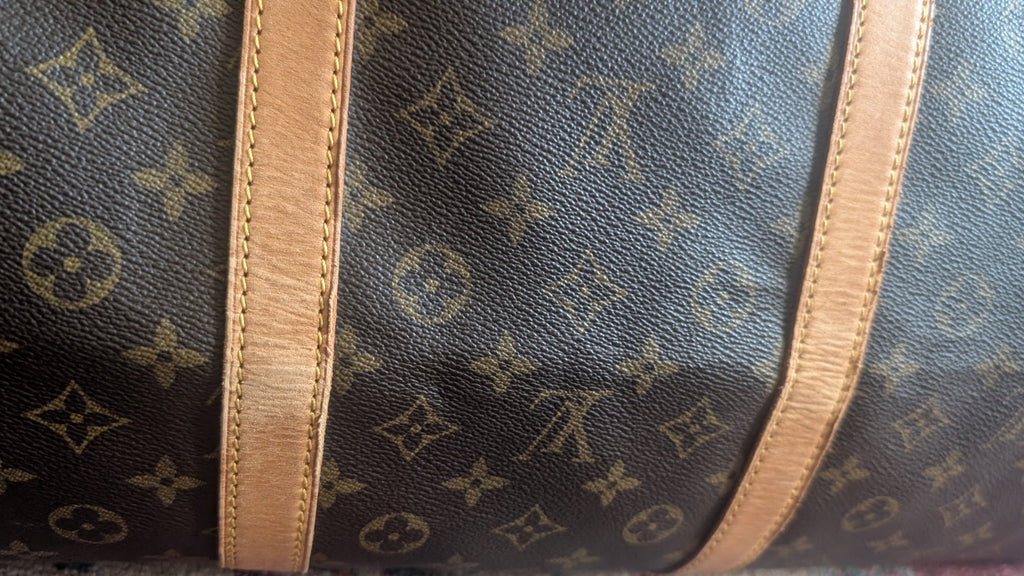 Close-up of a Louis Vuitton monogram canvas bag with tan leather trim, showing the classic dark brown and beige pattern. Pre-Owned Louis Vuitton Keepall Bandoulière 60 Monogram Travel Bag