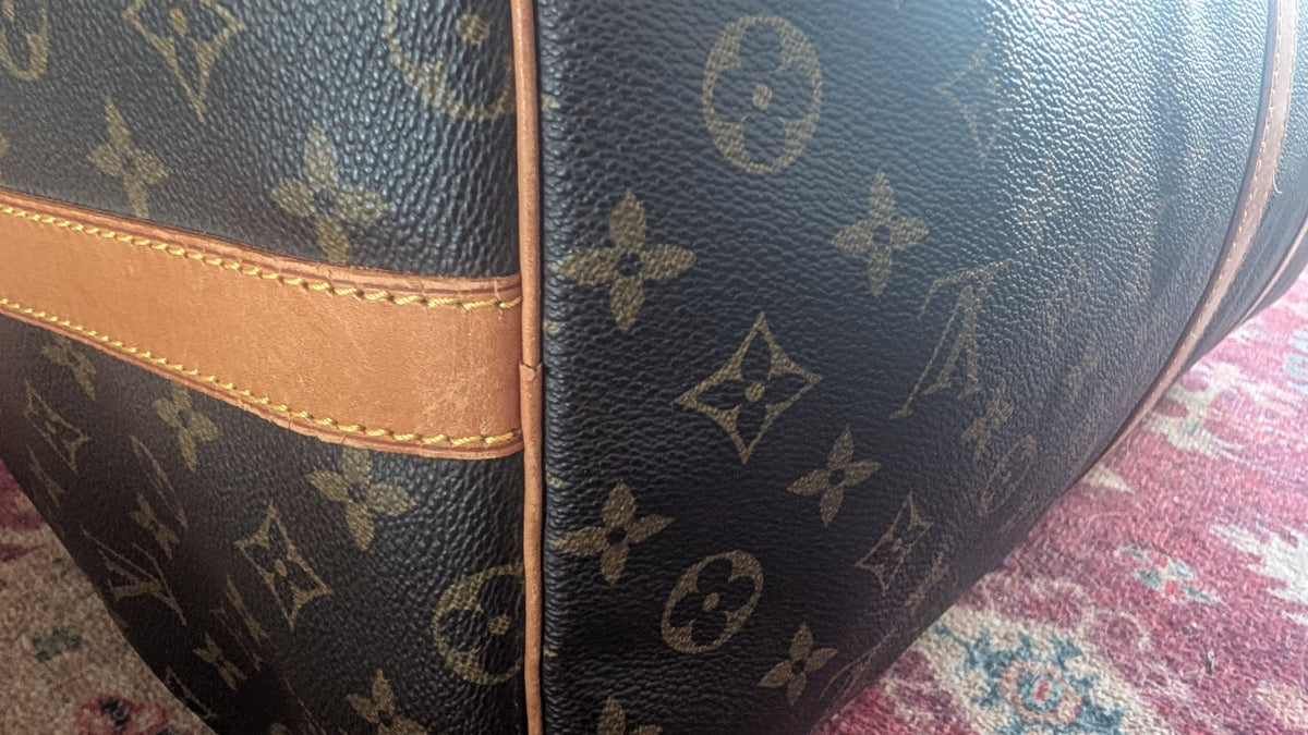 Close-up of a Louis Vuitton monogram canvas bag corner showing the dark brown coated canvas with tan monogram print and a tan leather trim strip. Pre-Owned Louis Vuitton Keepall Bandoulière 60 Monogram Travel Bag