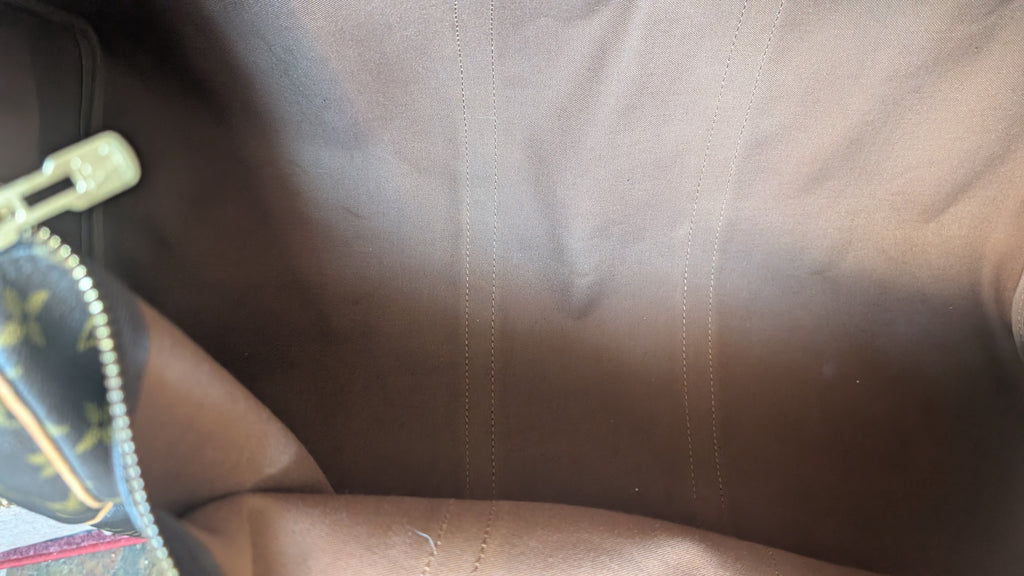 Close-up of a brown leather or faux-leather surface with visible stitching, a zipper pull, and part of a patterned fabric item at the left edge. Pre-Owned Louis Vuitton Keepall Bandoulière 60 Monogram Travel Bag